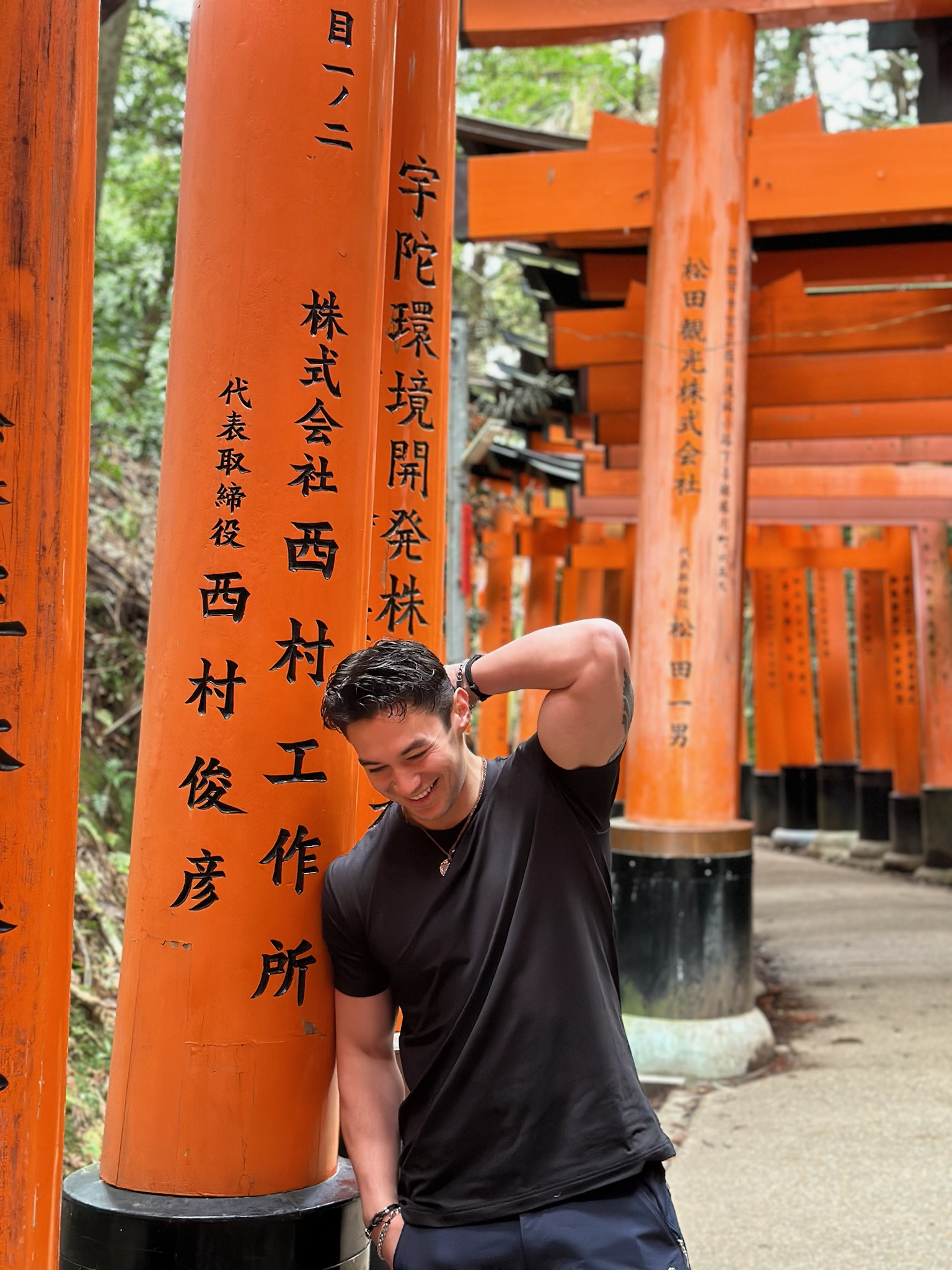 A man smiling and leaning against a red pillar in Tokyo, Japan.