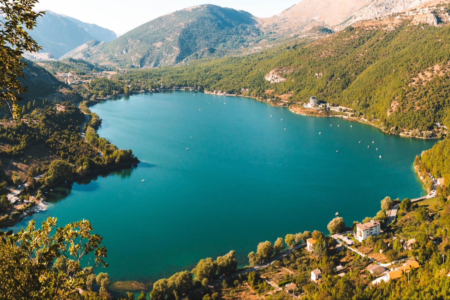 A view of a turquoise blue lake surrounded by trees and rocky mountains.