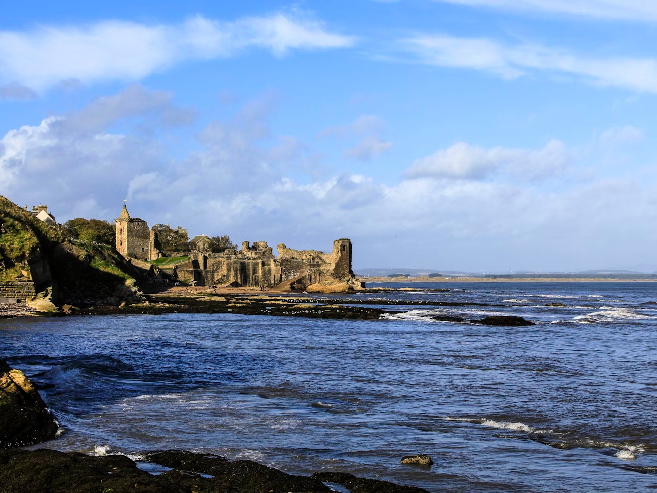 A view of the rippling blue sea in Scotland, with stone castles and rolling green hills in the background.