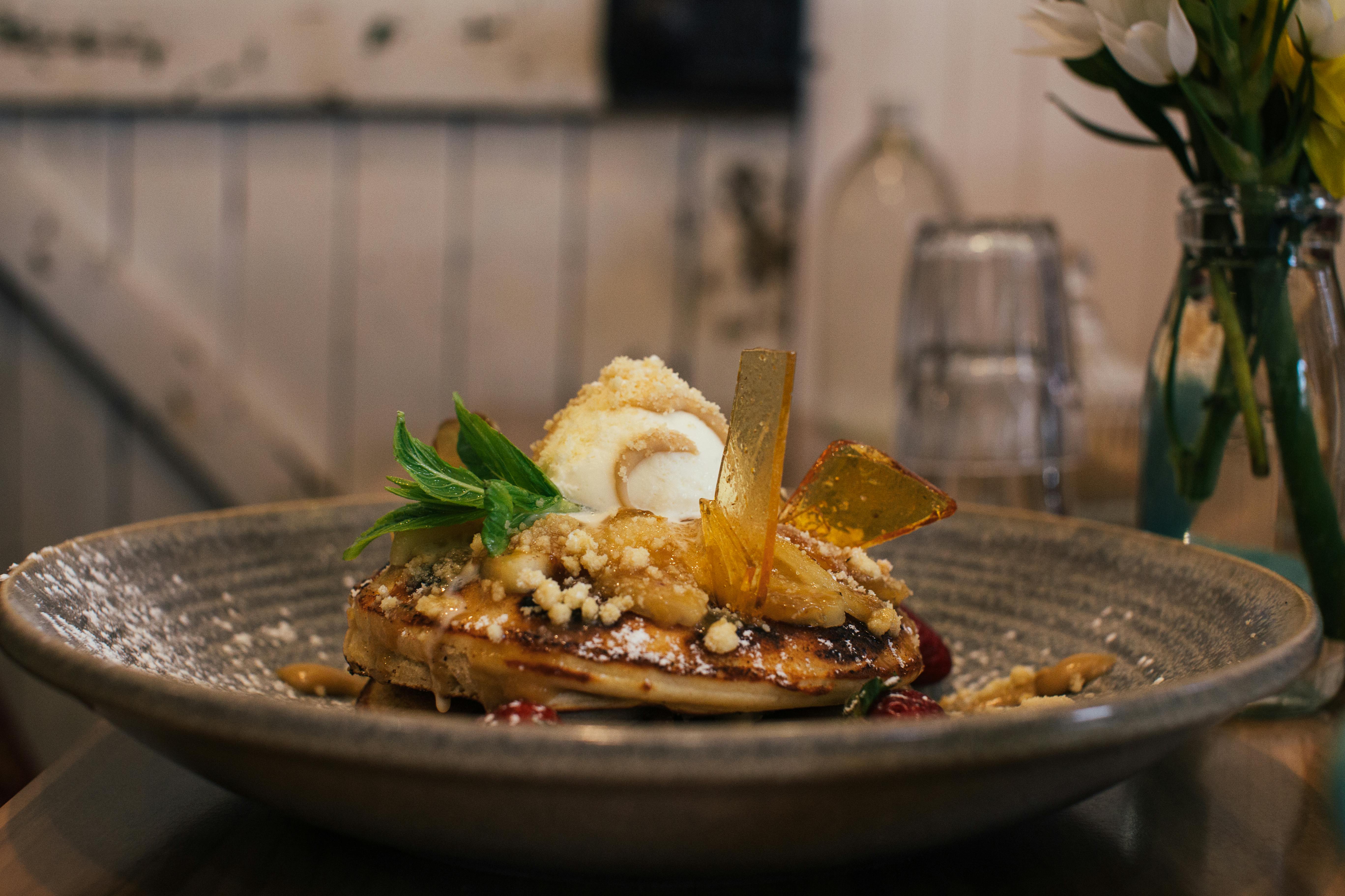 A plate of pancakes topped with gelato and caramel syrup on a wooden table in a farmhouse-style setting.