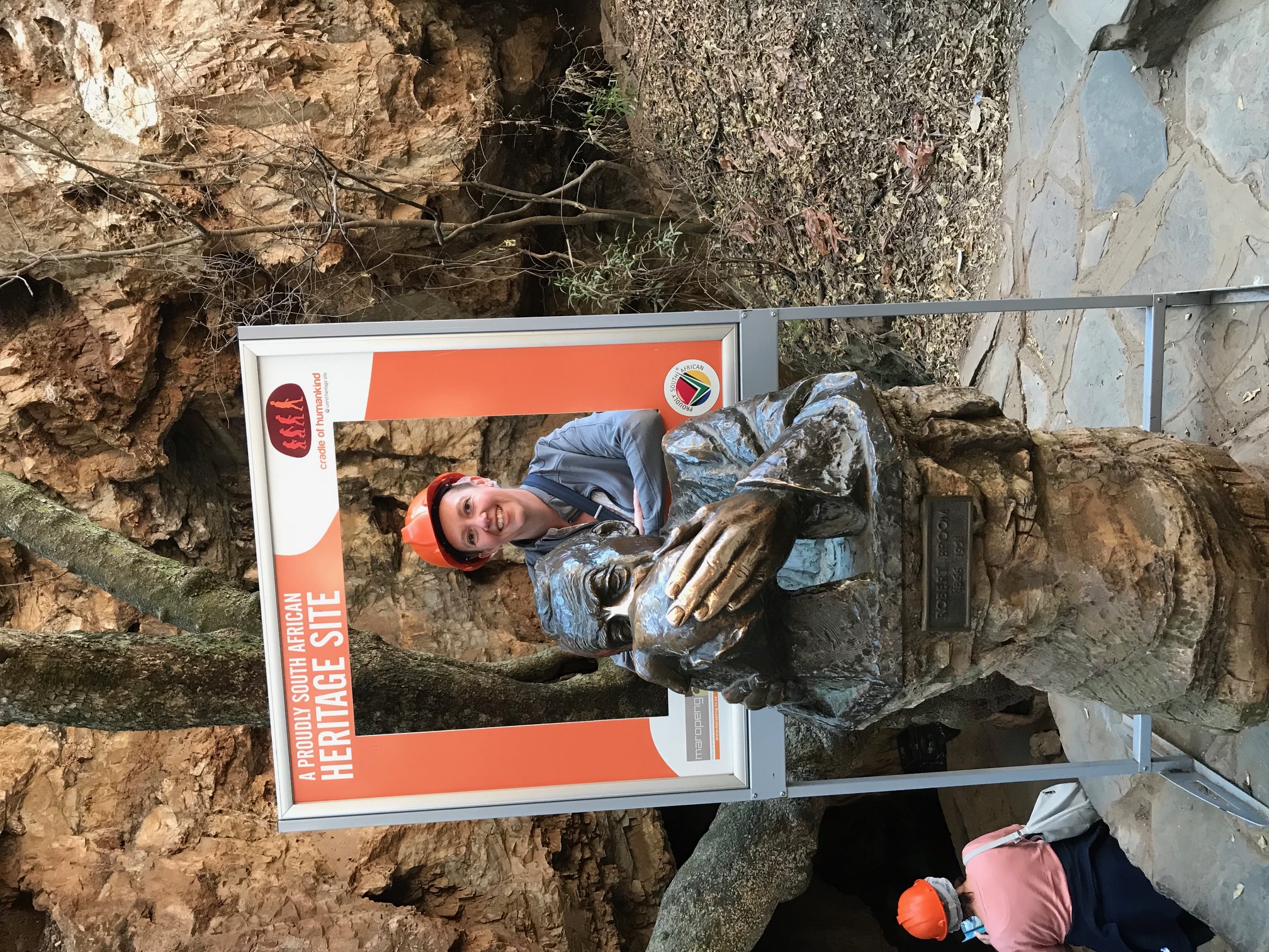 Travel advisor Tammy in an orange helmet posing with photo props and a statue outside with rocky landscape in view
