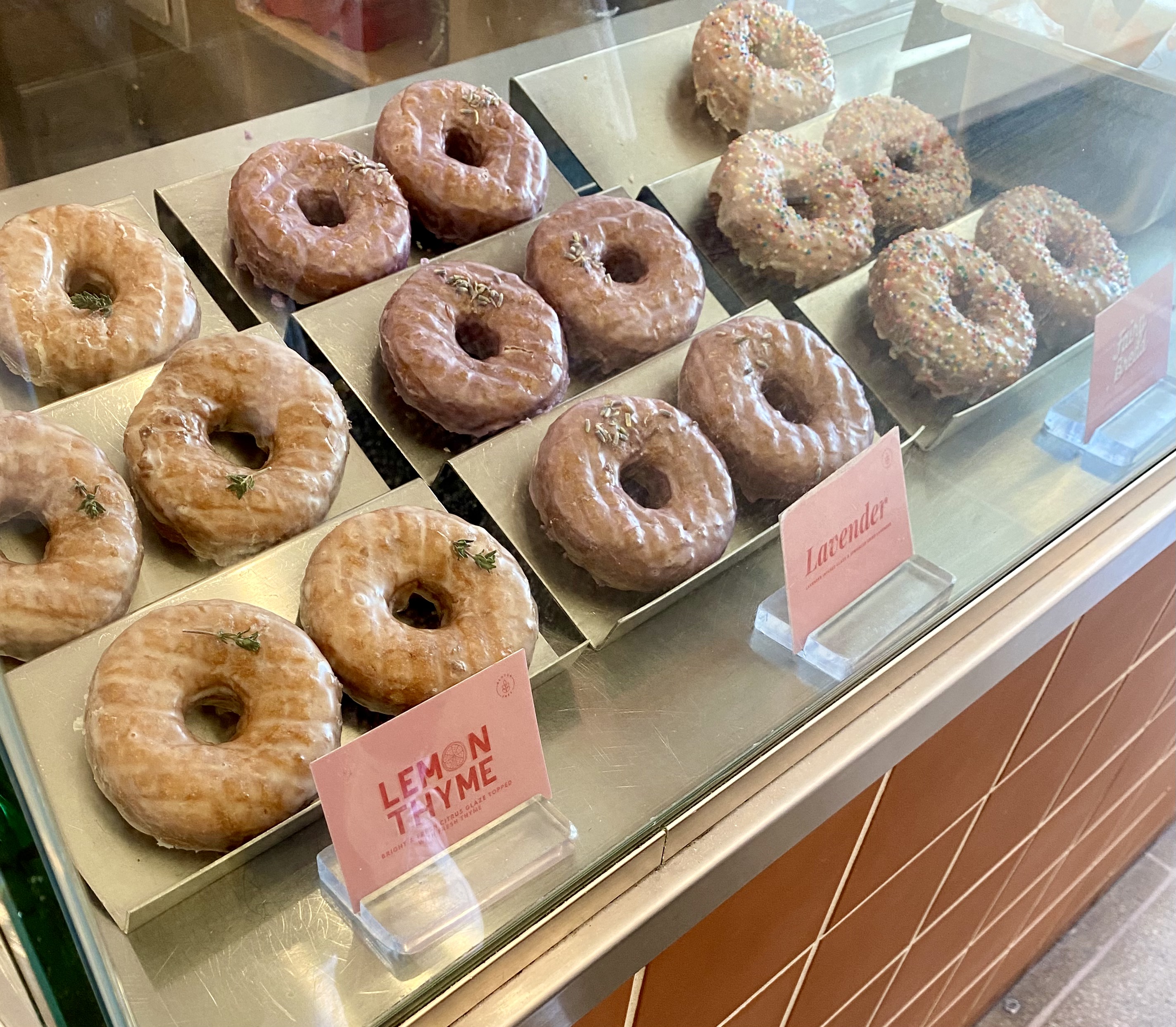 A glass case full of donuts with pink notecards with flavor labels in front of them.