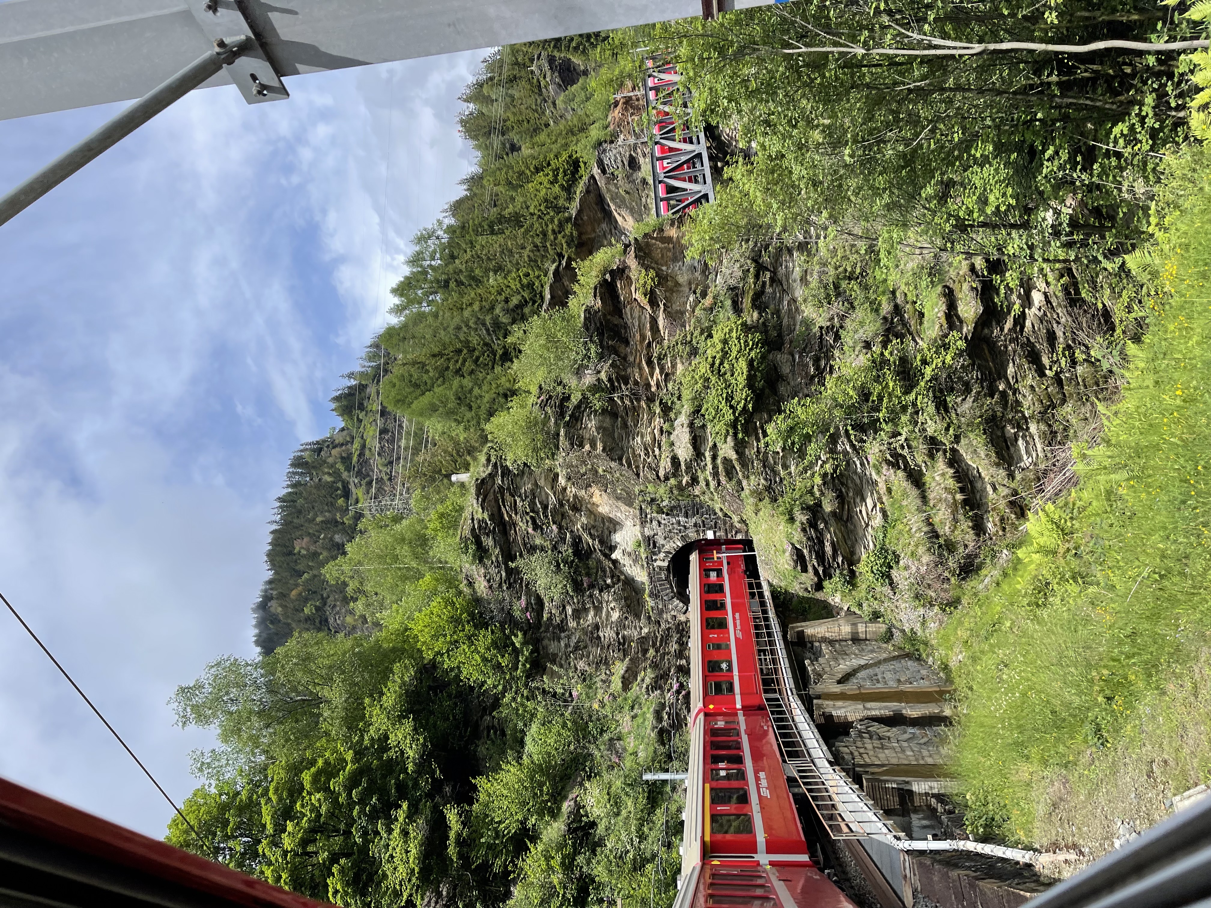 A red train on an elevated mountainside bridge traveling through a tunnel.