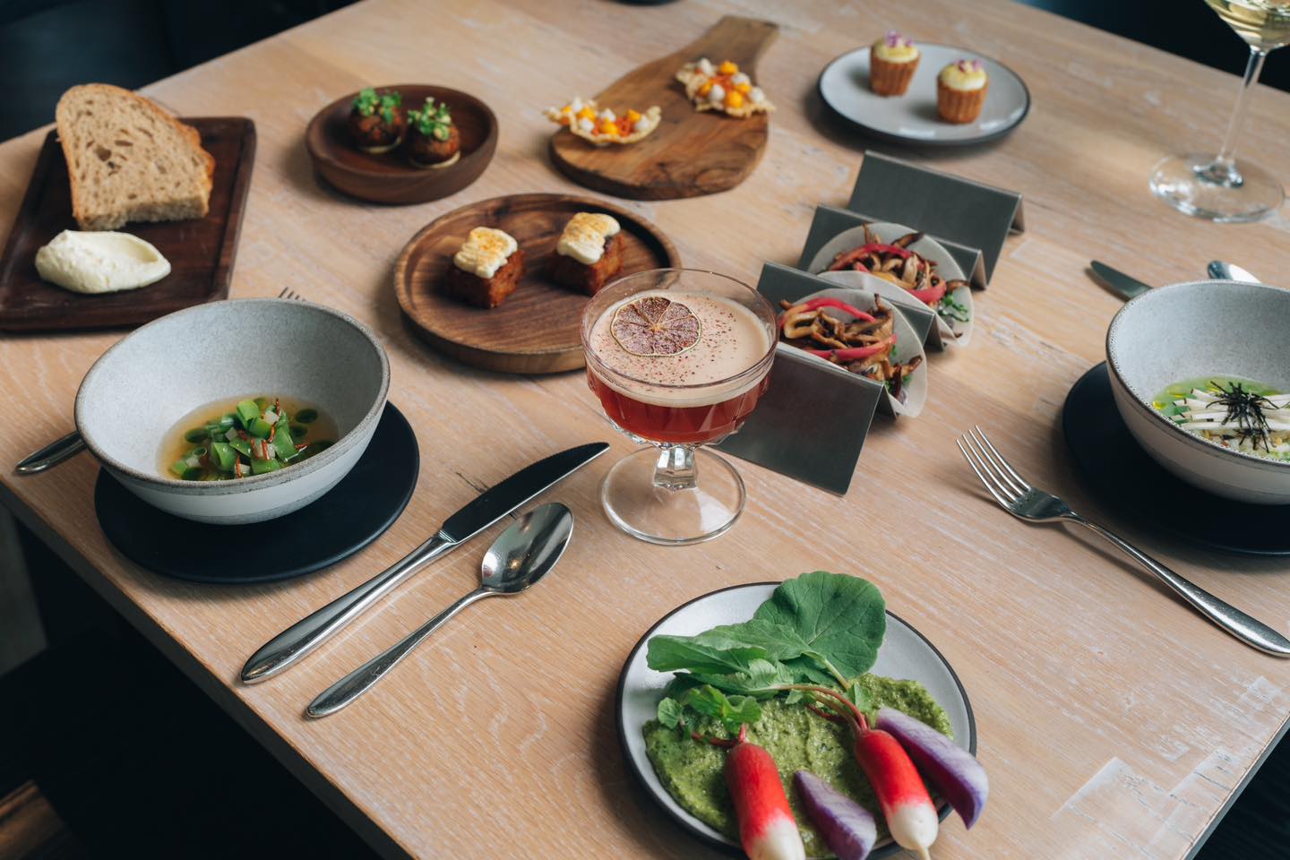 A wooden table full of various plates and platters of food. There is also flatware and drinking glasses.