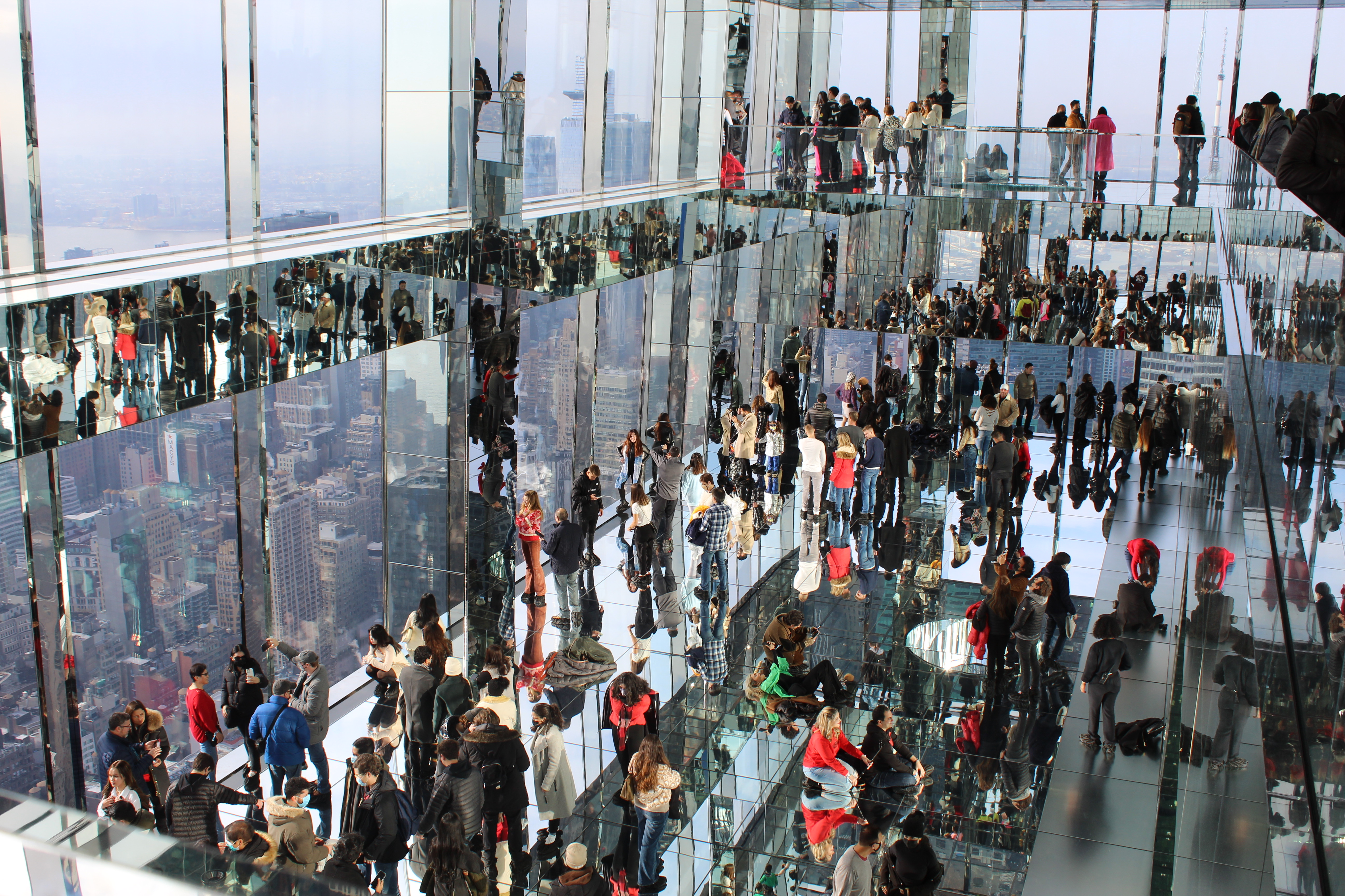 A view of people walking around a reflective building with large glass windows and mirrored walls.