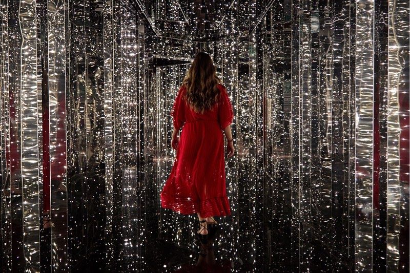 A woman in a red dress walking down a hallway lit up with twinkling lights.