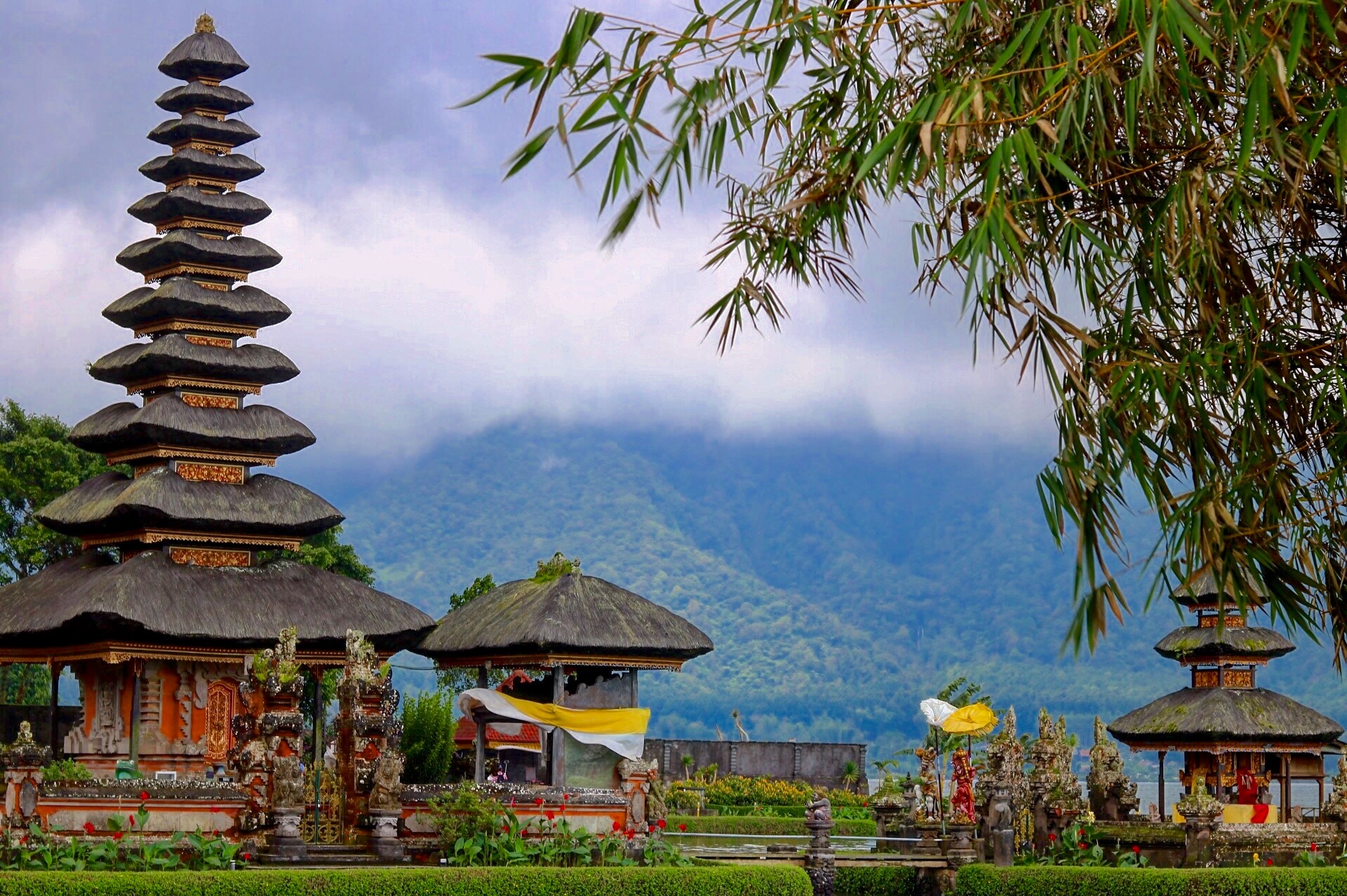 Three temple buildings with a mountain in the background and a tree in the foreground.
