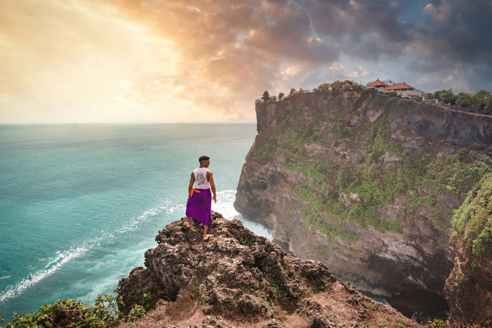 A person standing on a cliff at the ocean's edge.