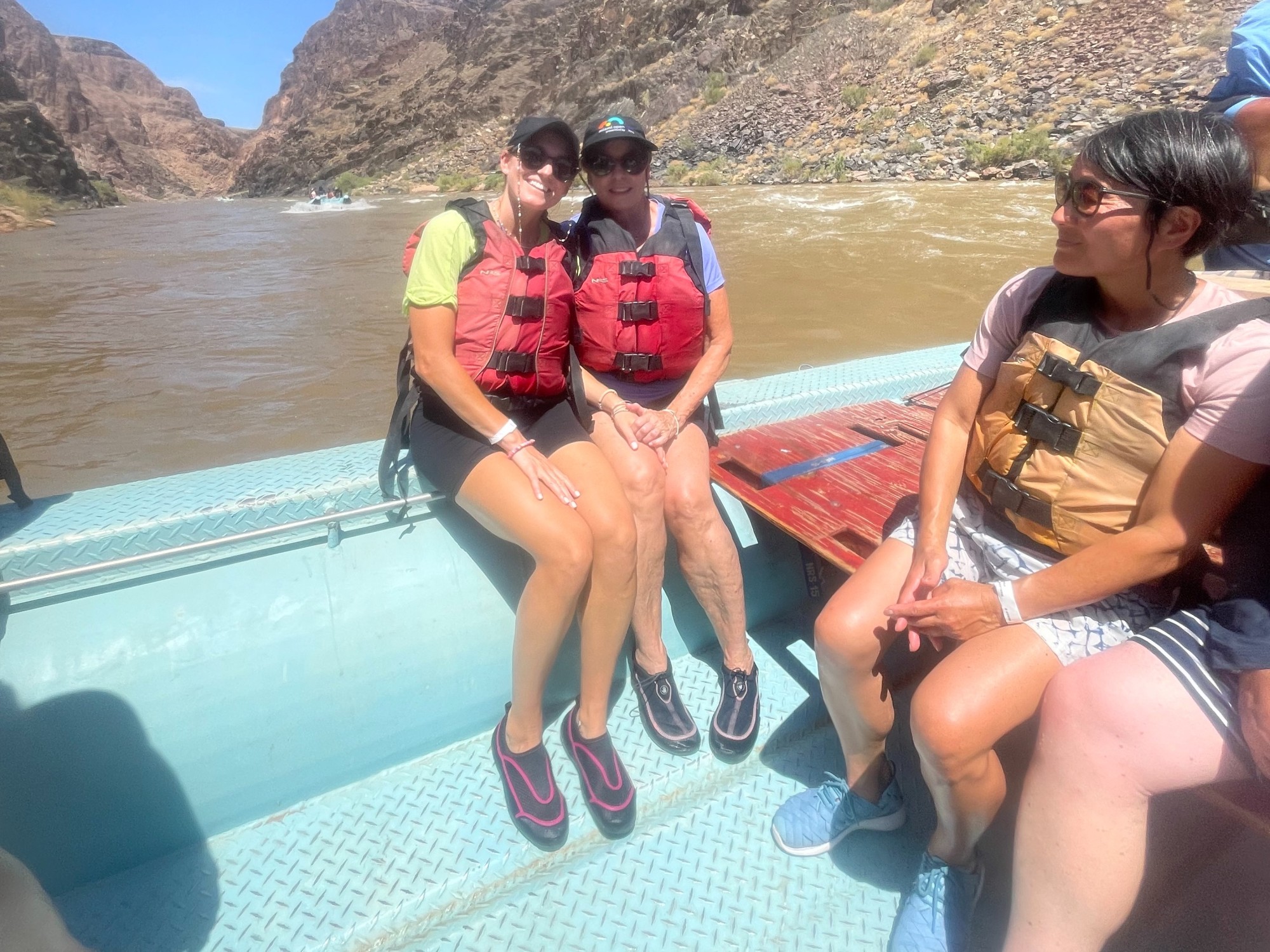 Two women in life jackets on a blue raft in a river, with other people next to them.