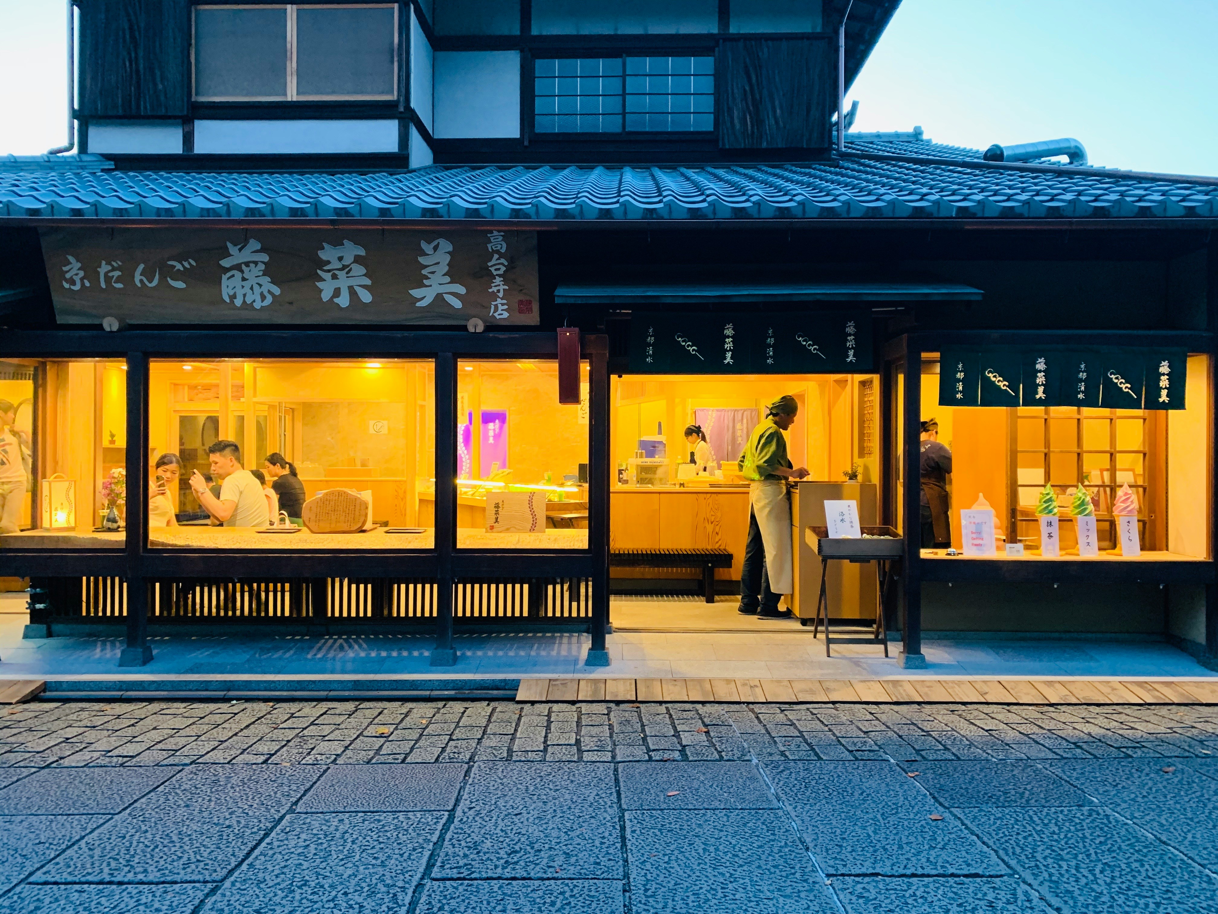 A picture of a person standing beside a table at a restaurant. The photo is taken from the outside with a sign and a stone path.