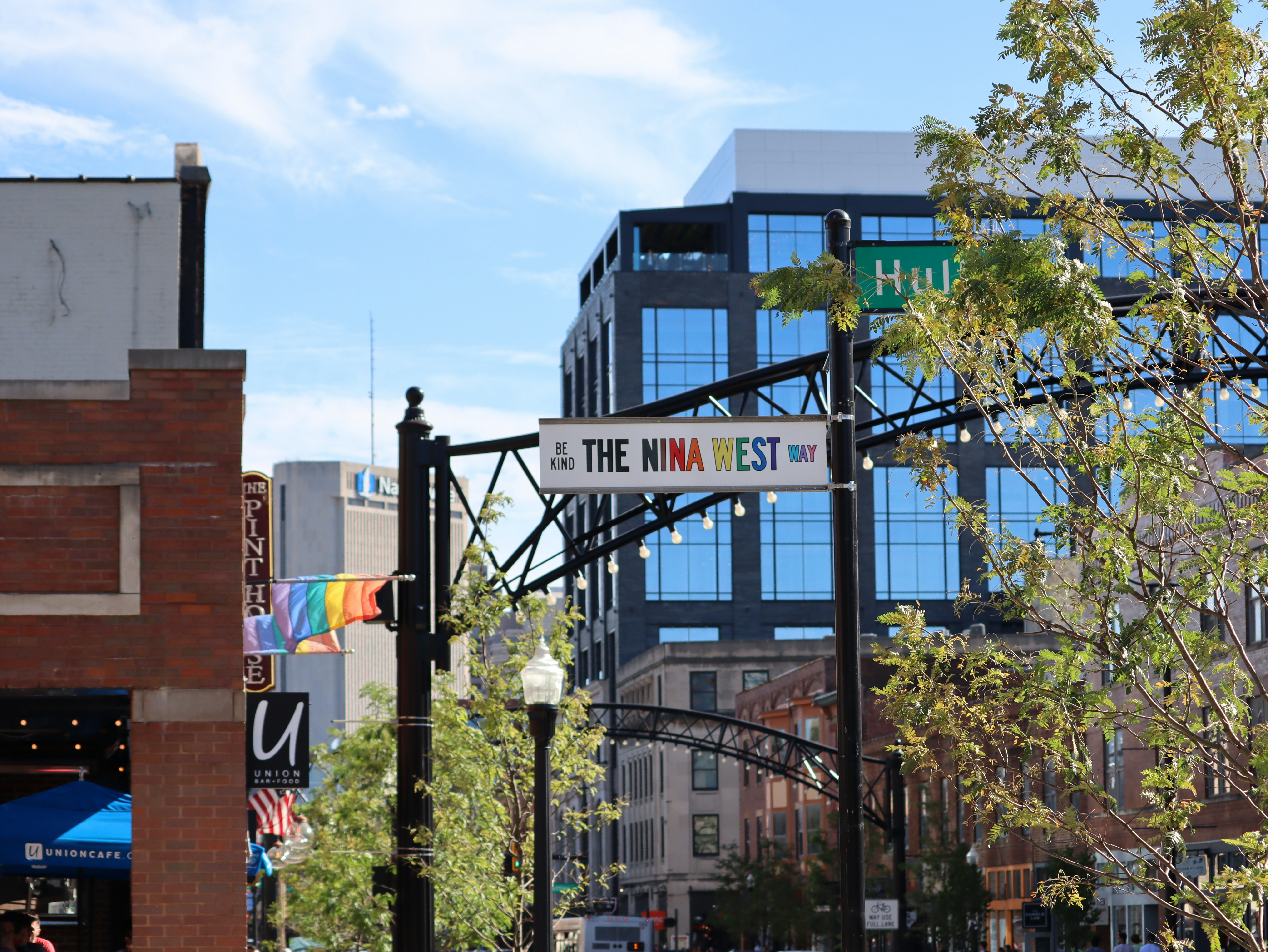 An aerial view of a street sign that reads "The Nina West" on a pole on a city street during daytime.