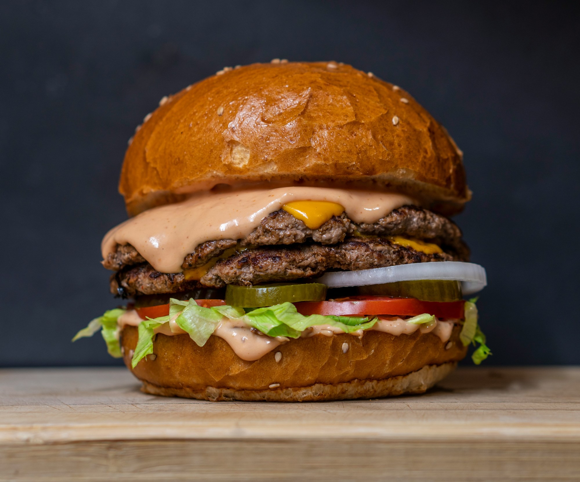 A double patty meat burger on a wooden platter.