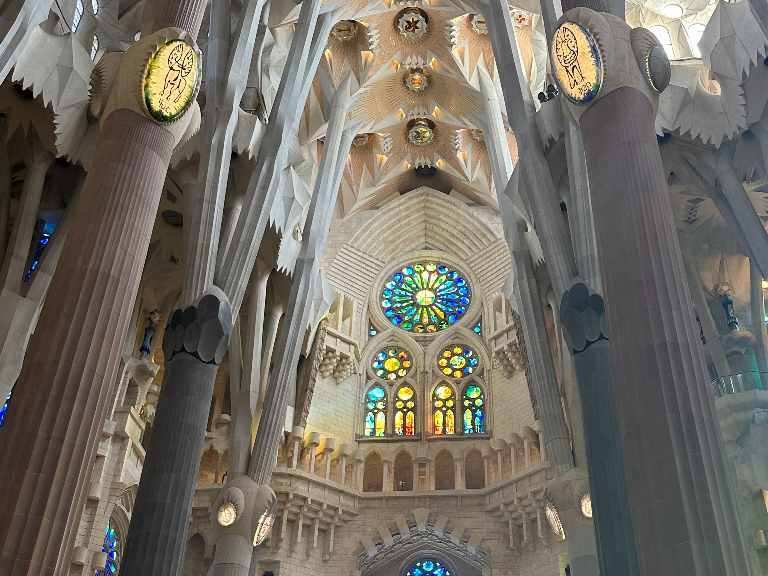 A breathtaking view of the white stone architecture of the inside of the La Sagrada Familia with blue, green, red and gold stained glass windows.
