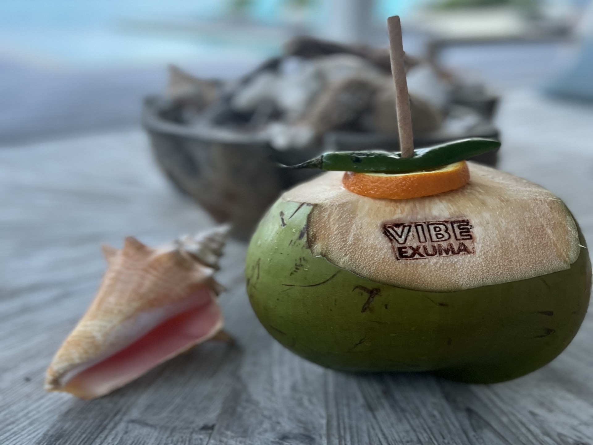A picture of a coconut cocktail with "Vibe Exuma" carved into it placed on a table.