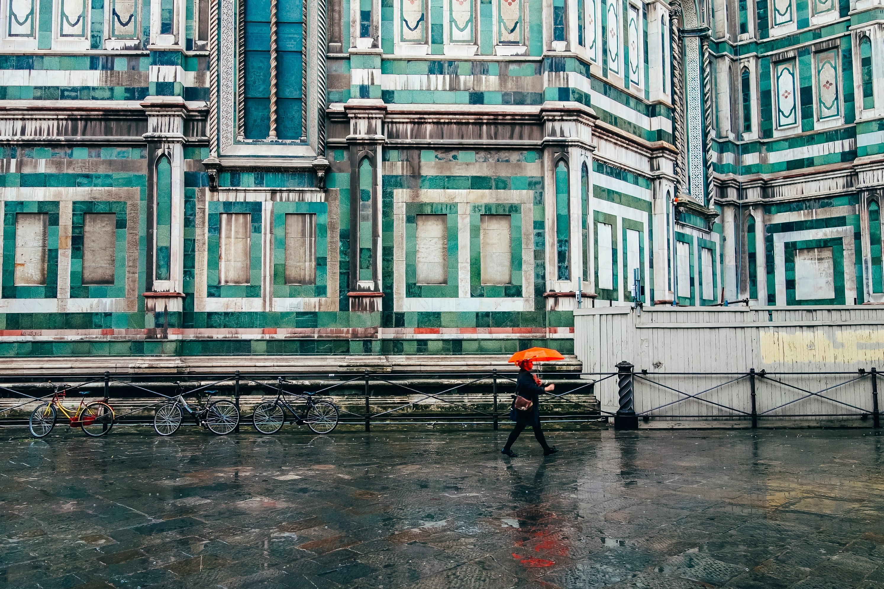 a picture of the streets of Florence in front of a green and blue tiled building during daytime.