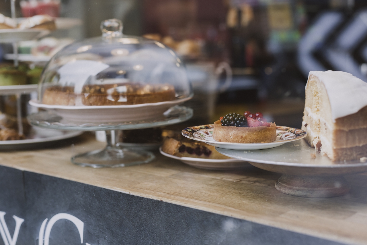 tarts and cakes sit on display stands on a wooden bar