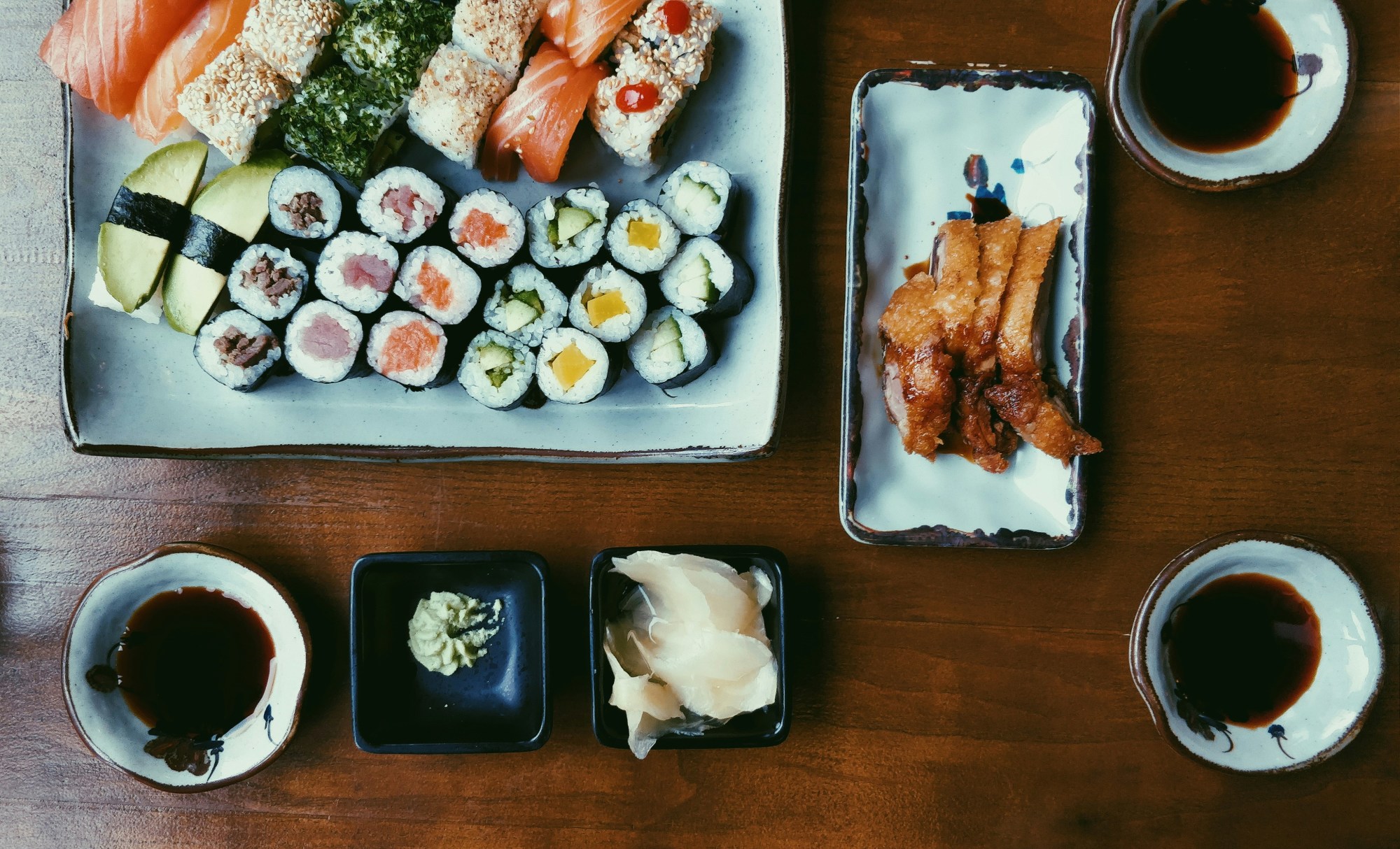 An overview of sushi, soy sauce and protein on top of a wooden table.