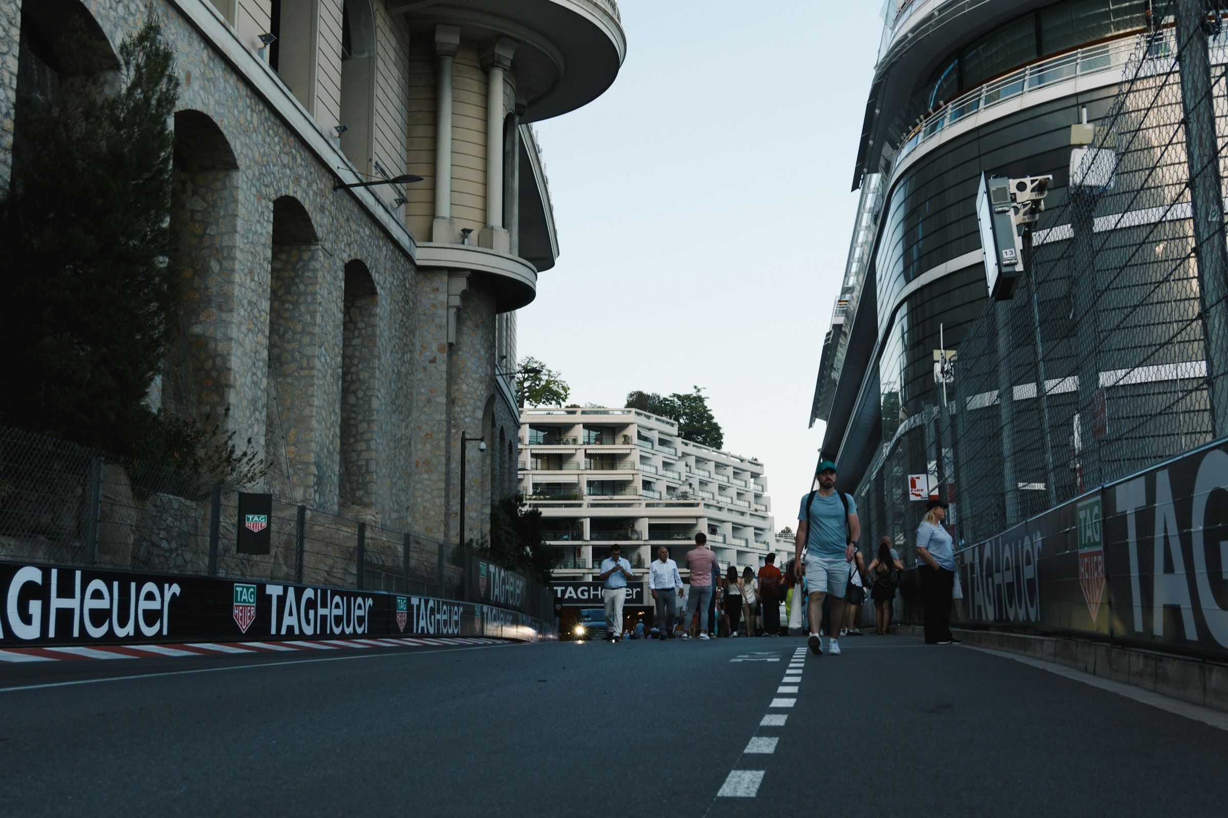 A street view of the tunnel exit at Monaco Grand Prix Circuit surrounded by stone buildings and modern architecture, as well as people walking down the road in the distance.