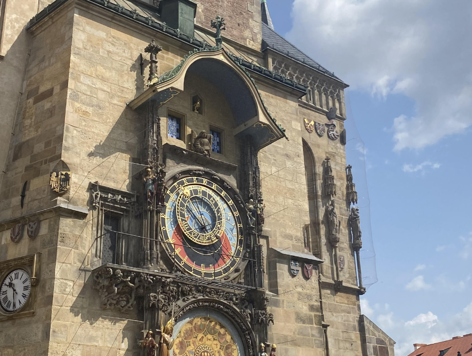 A view of the astronomy clock tower in Prague. It's a large, stone building with blue, yellow and red detailing.