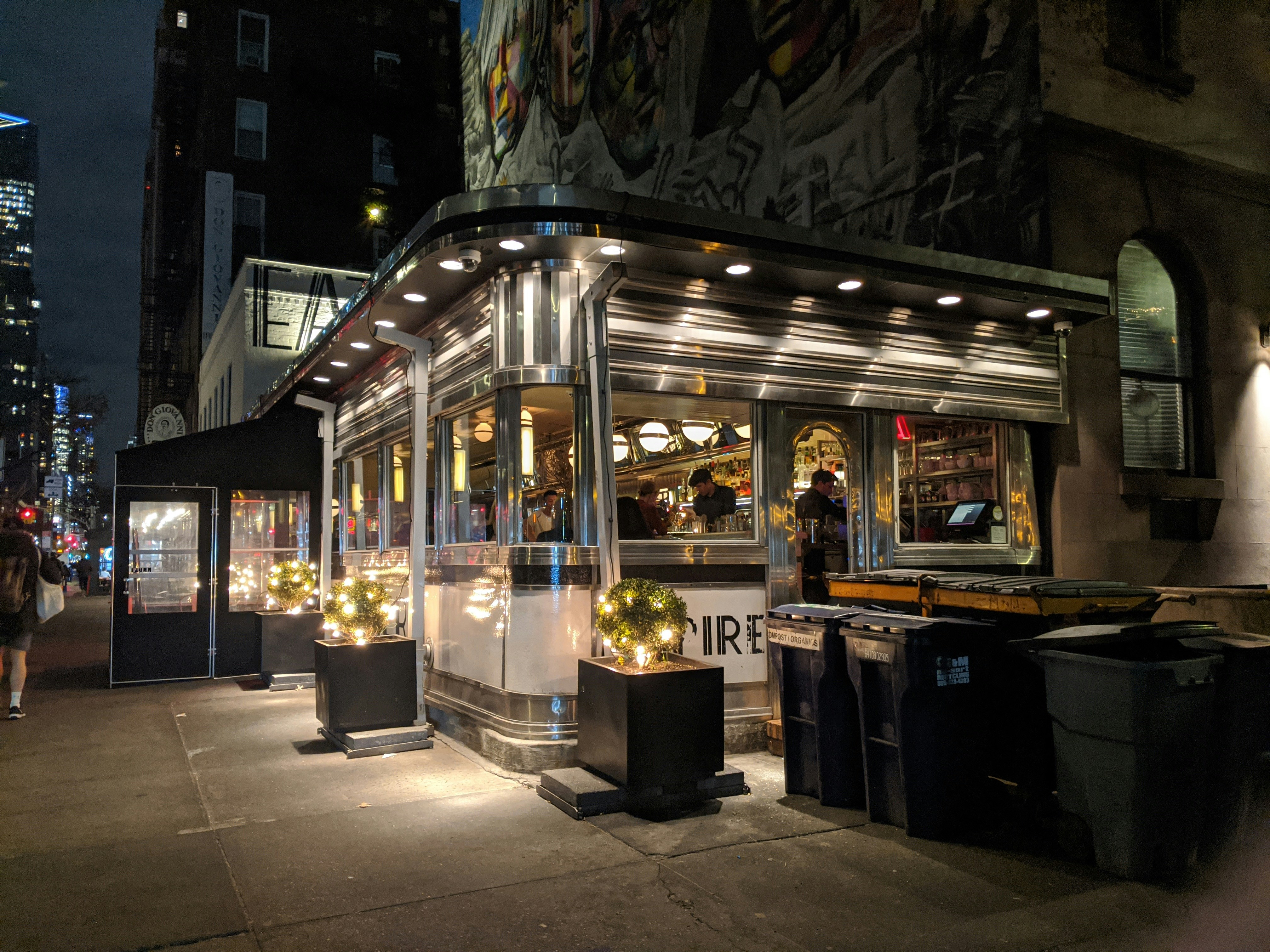 A picture of people dining inside of a restaurant at night on a city block corner.