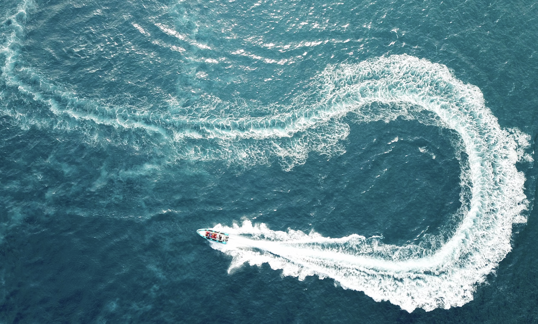 An aerial view of a yacht with curved waves over a turquoise blue body of water.