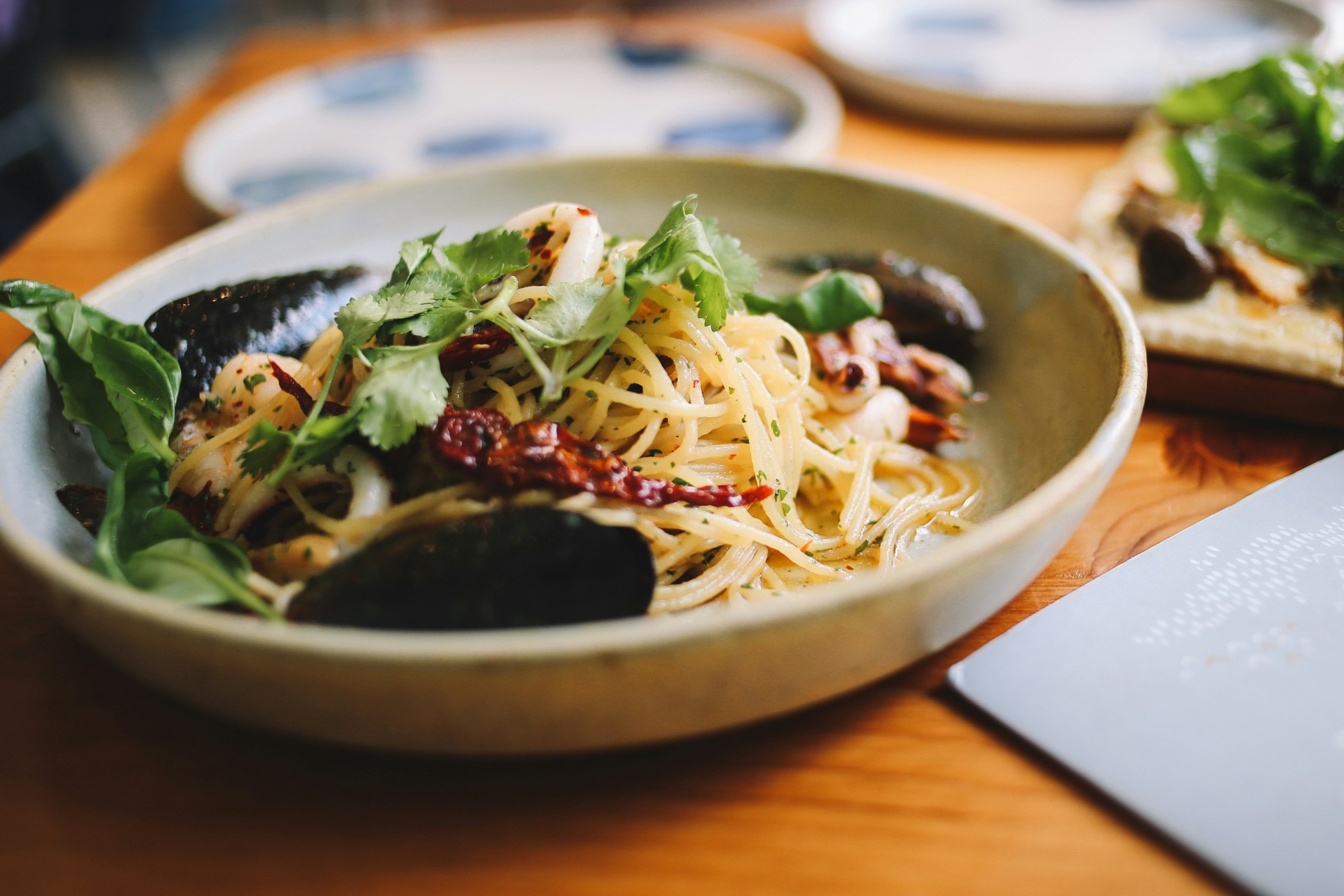 Seafood pasta dish on a wooden dinner table with other plates surrounding it