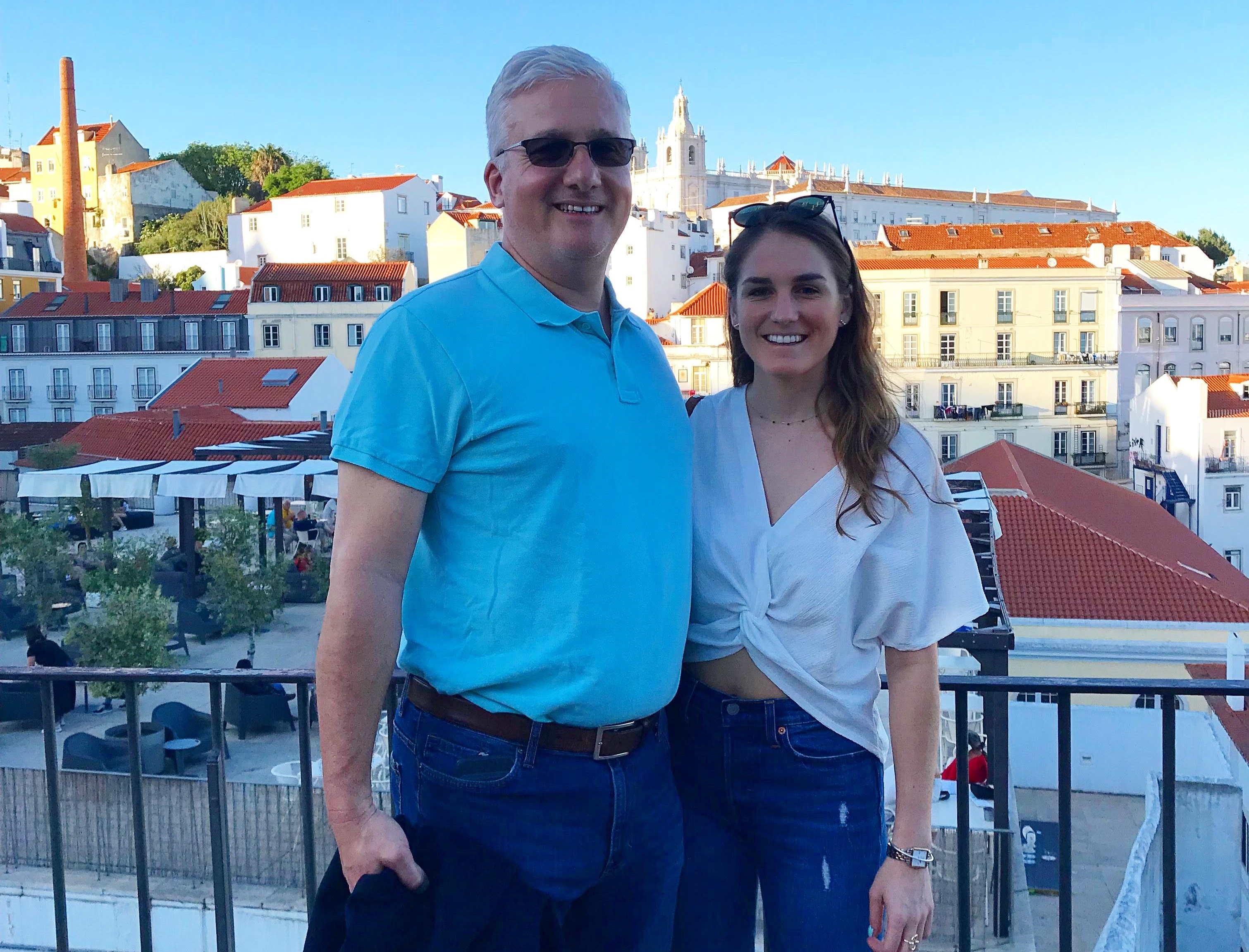 A photo of Tori and her Dad standing on a deck with the beautiful views of Lisbon in the distance.