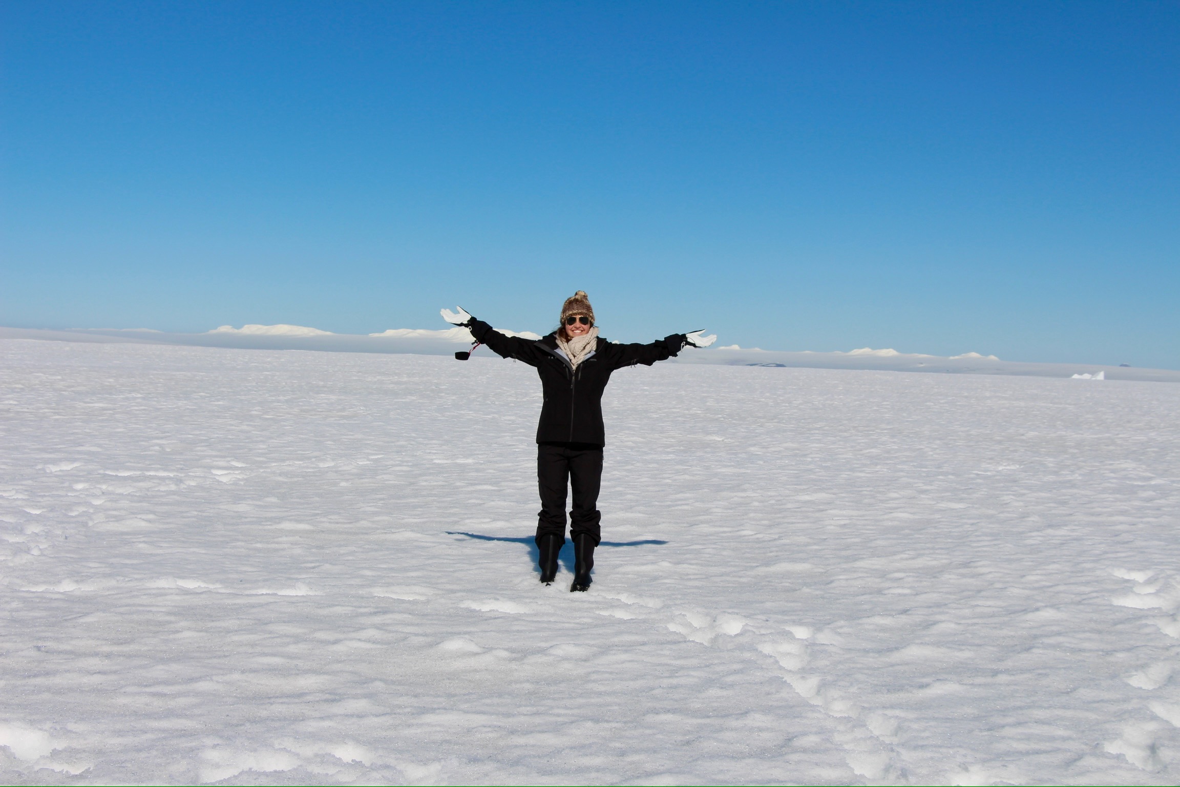 A woman standing on snowy terrain with her arms outstretched wide, posing for an image.