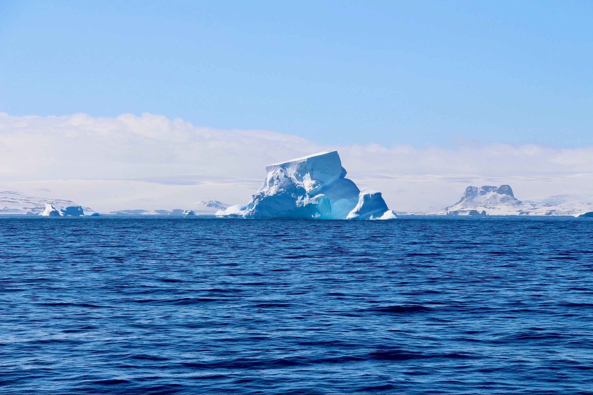 A view of an enormous ice berg in the middle of the rippling blue water during the daytime.