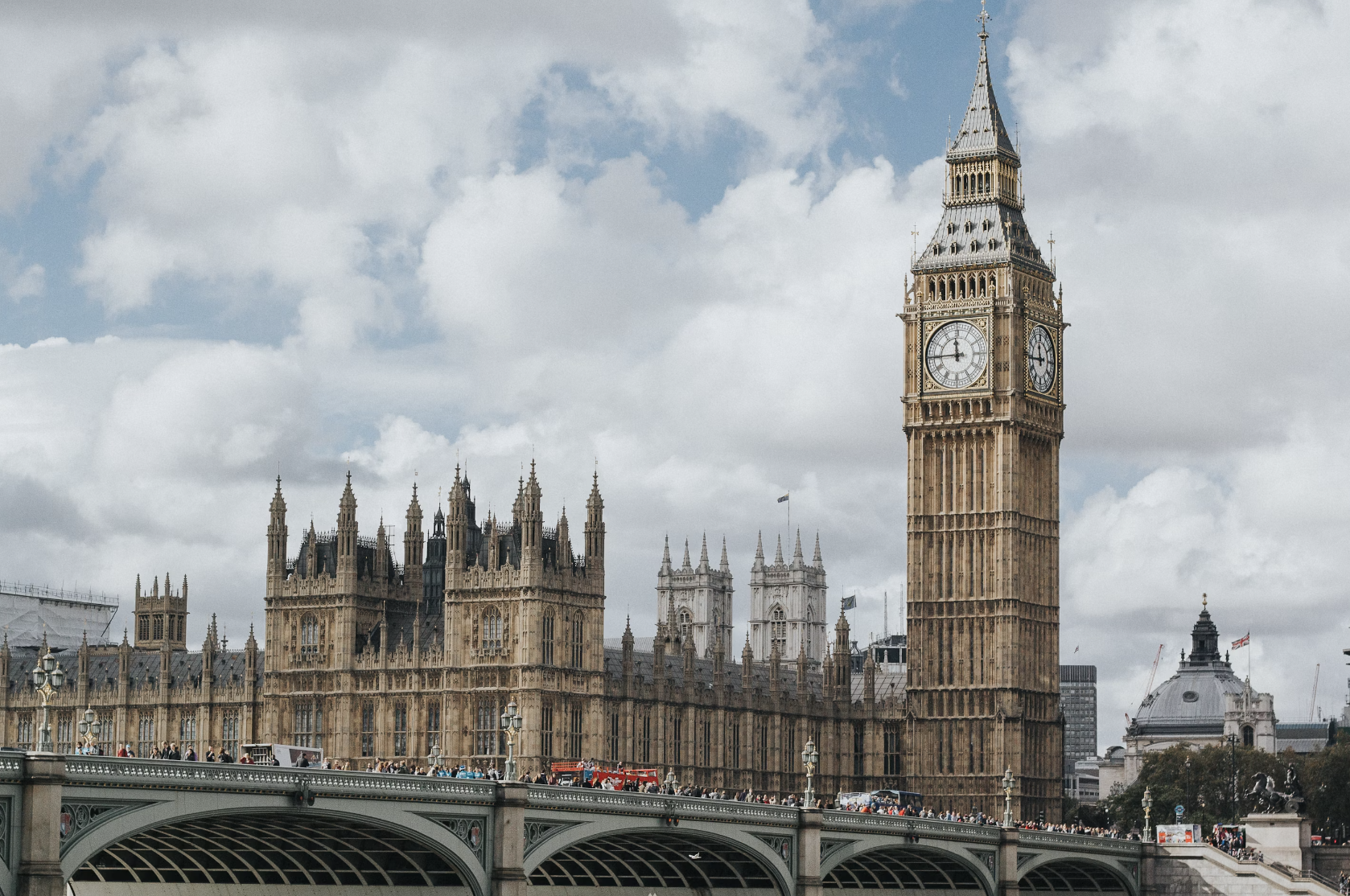 A photograph of Big Ben, a large clock tower and a bridge in London on a cloudy day.