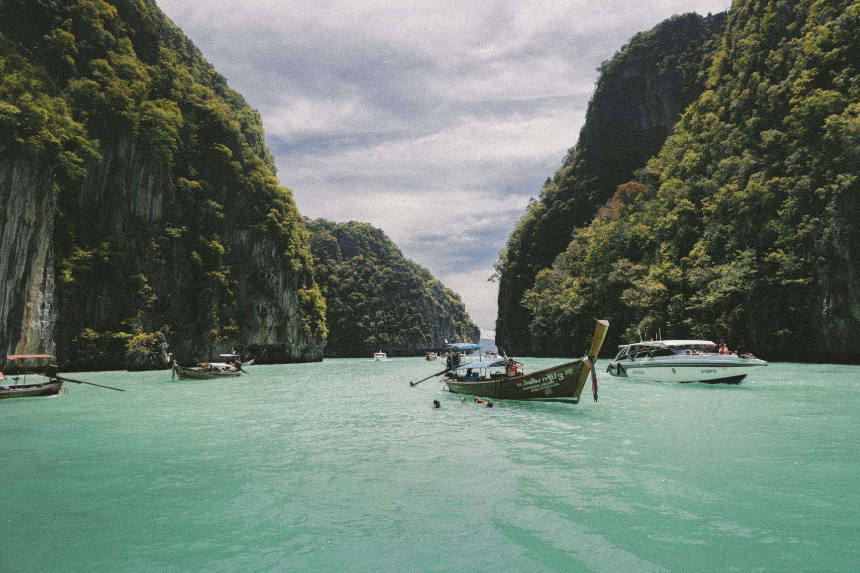 A view of boats sailing upon turquoise blue water surrounded by lush green cliffs.