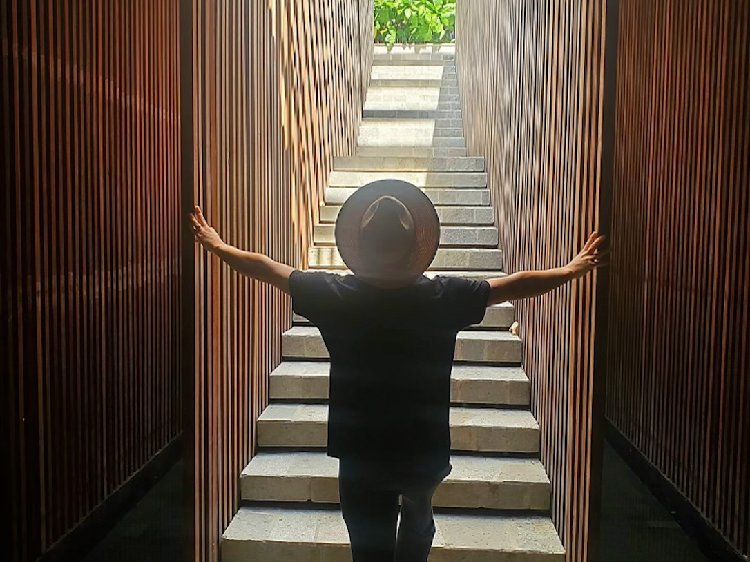 A person with their arms outstretched and hands grasping onto the wooden walls on the right and left sides of stone steps.