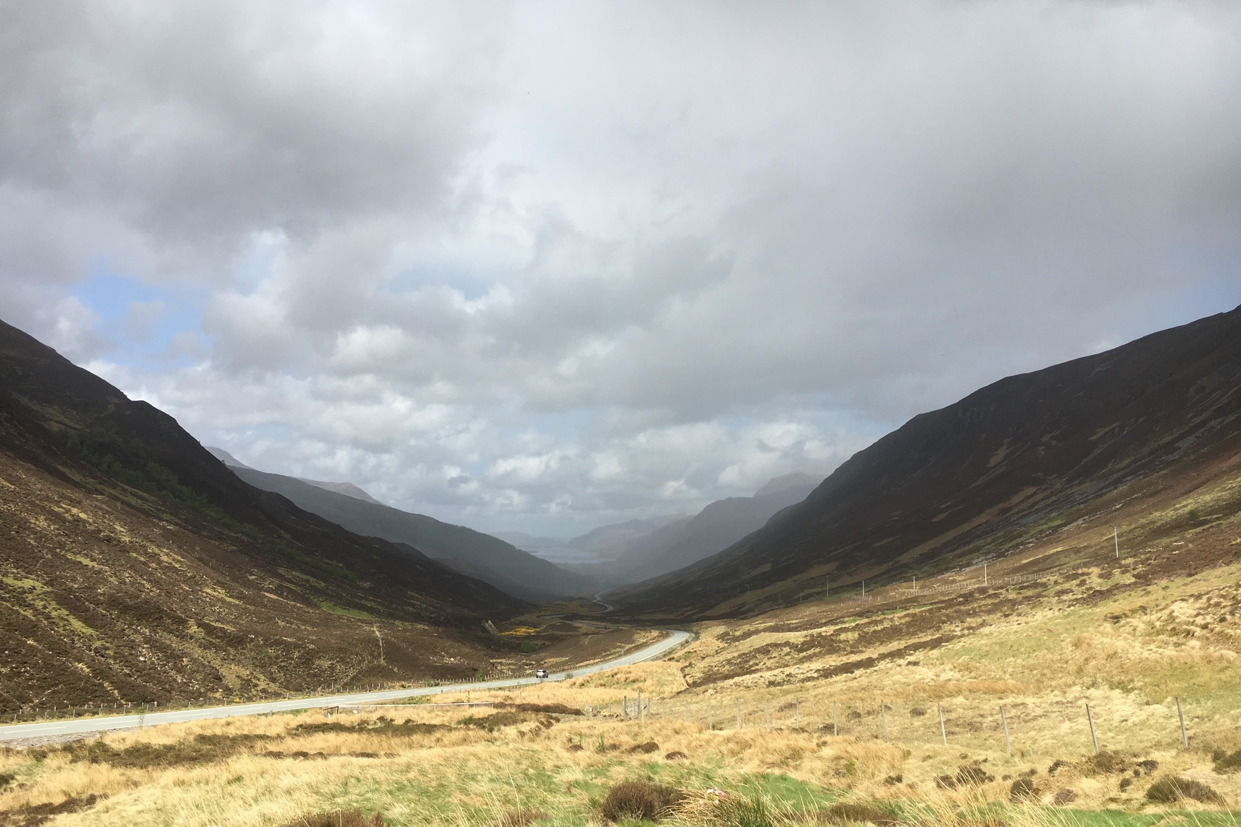 A view of dead grass and curved mountain ranges that fade into the cloudy fog.