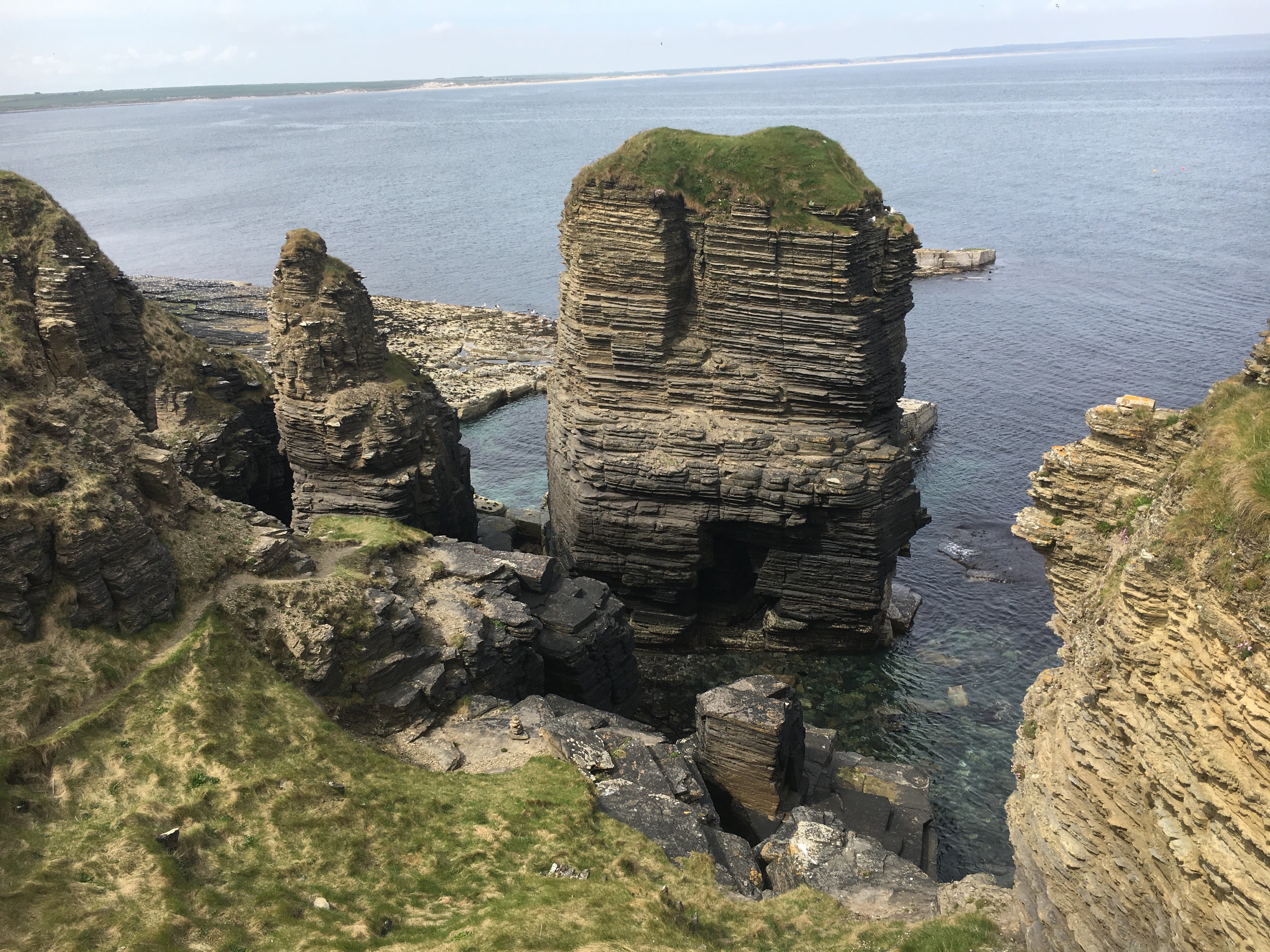 An overview shot of various rocky cliffs covered in grassy terrain and towering over the blue sea in the distance.