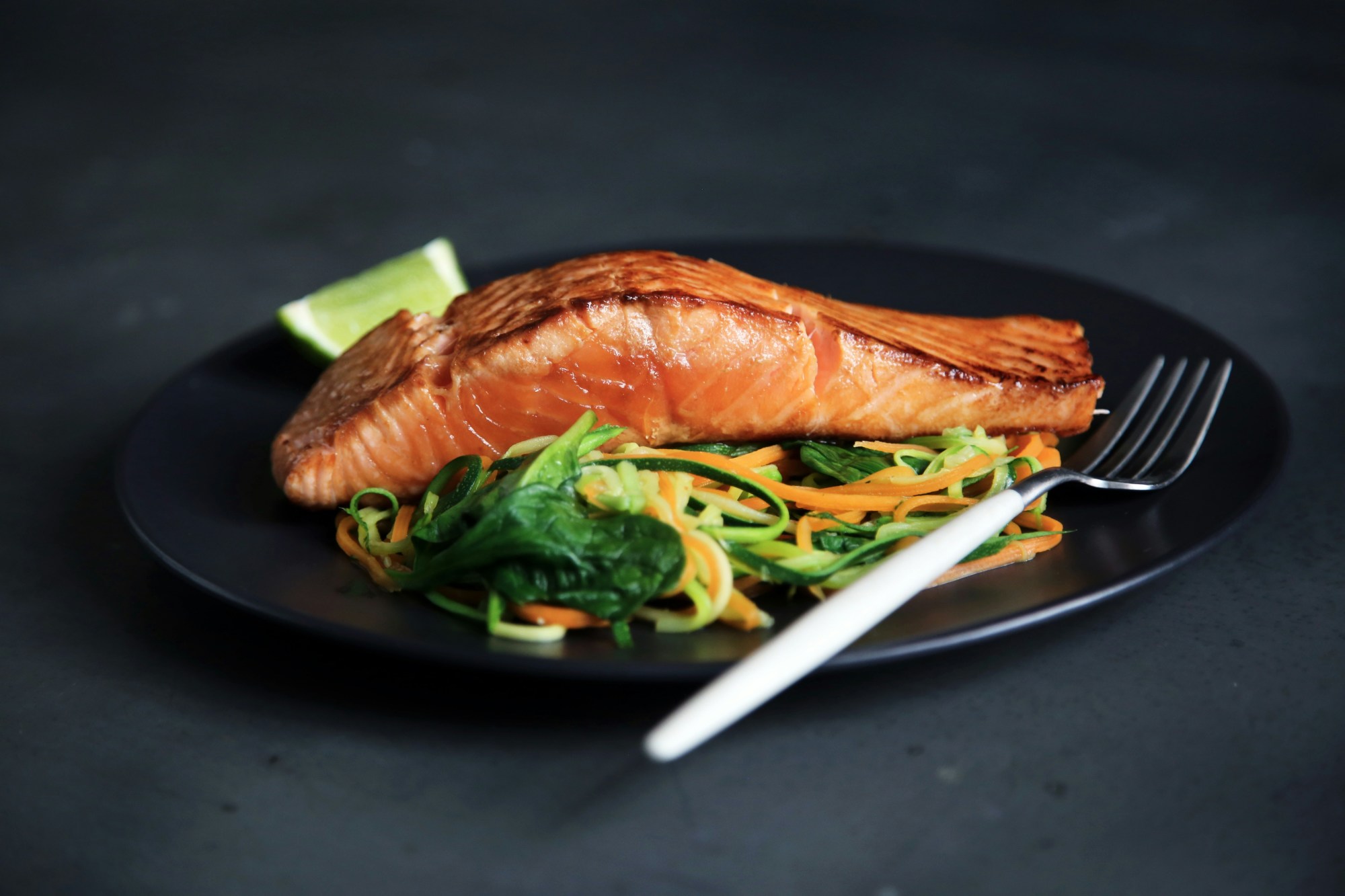 Grilled fish with vegetables on a black plate.