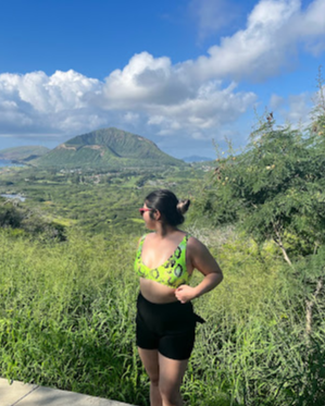 Claudine on a hike with a lot of greenery and a mountain in the distance.