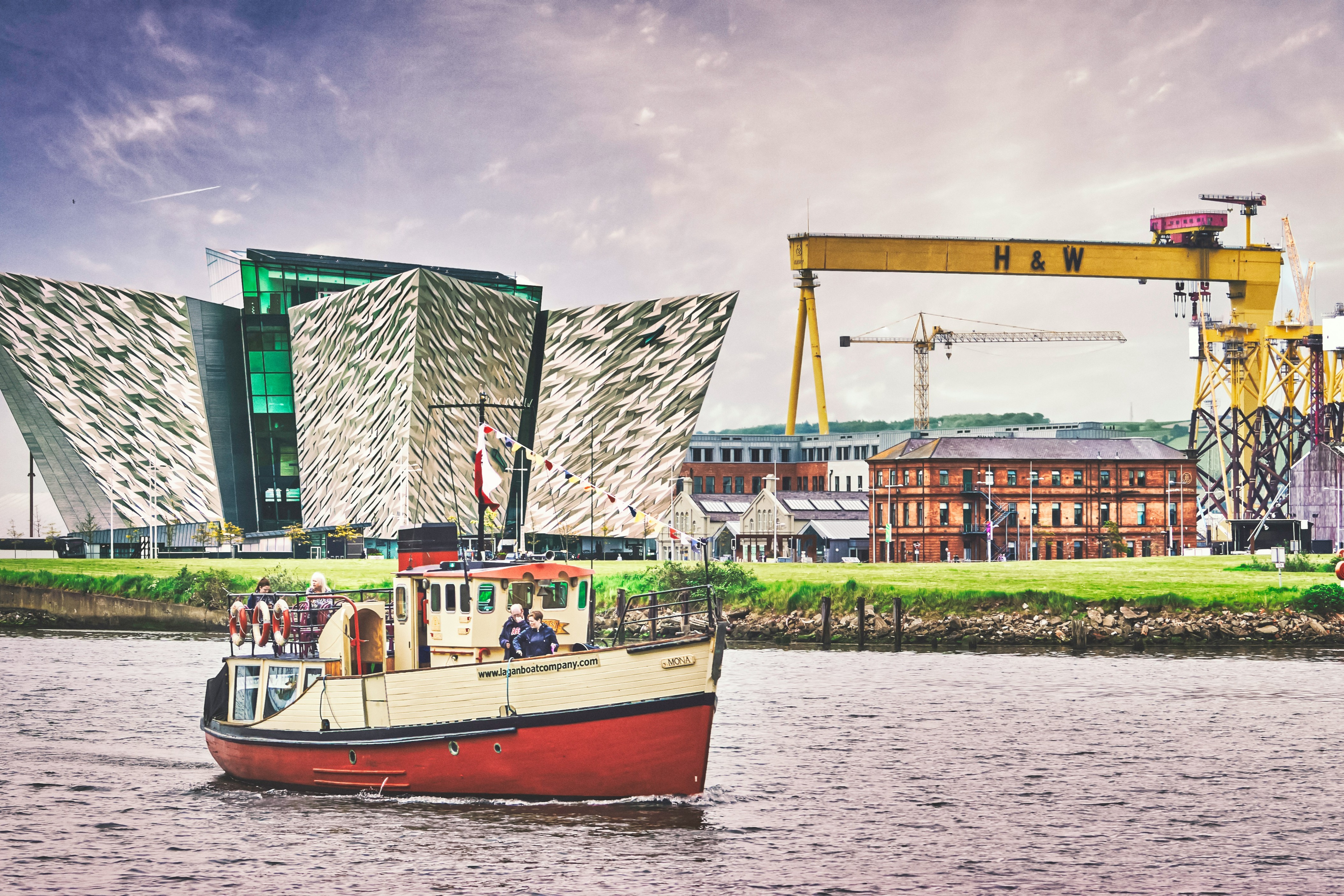 A red and white boat on water near green and white building.