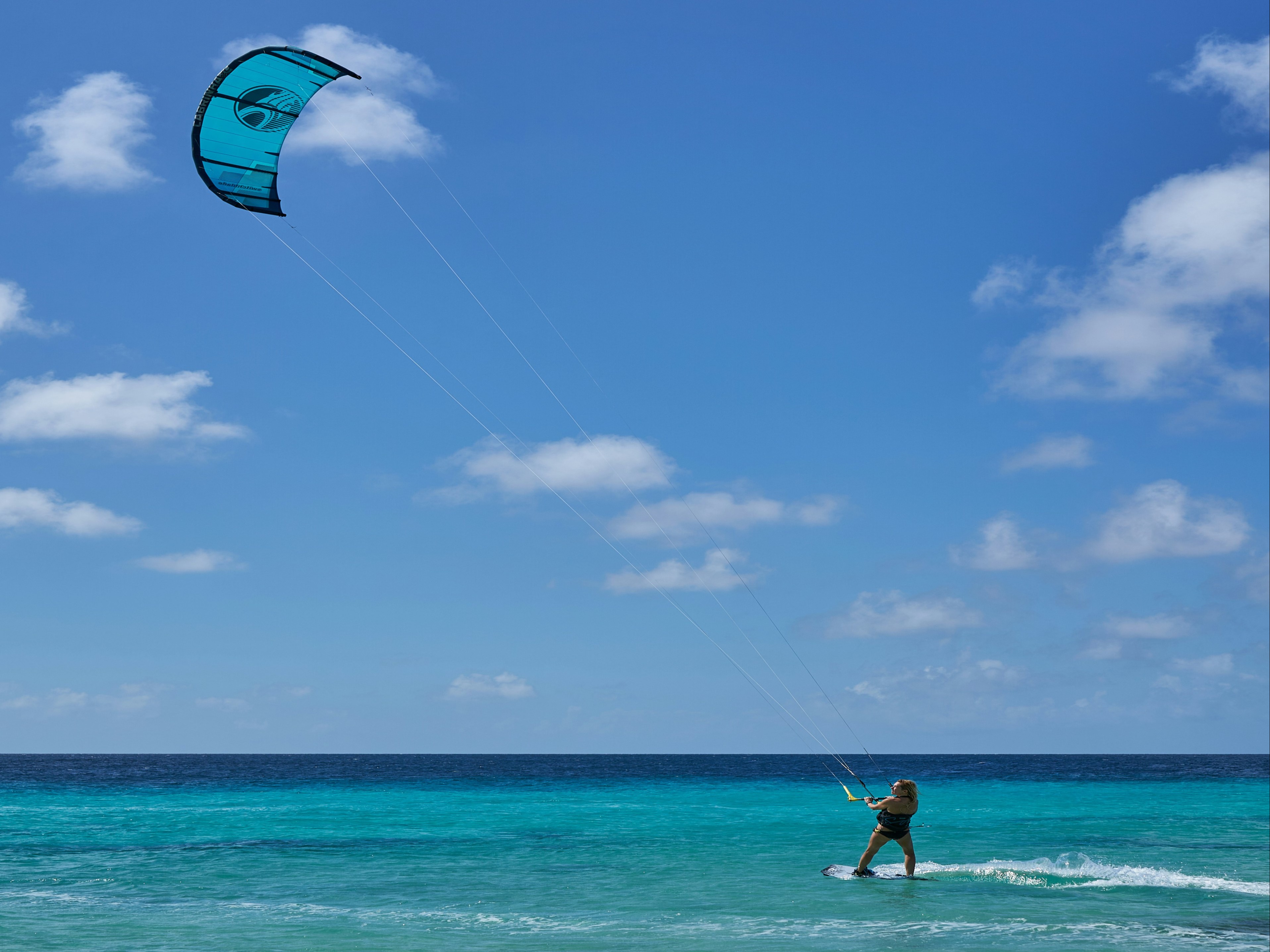 A picture of a woman in a swimsuit holding a blue and white kite surfing on the sea during the daytime.
