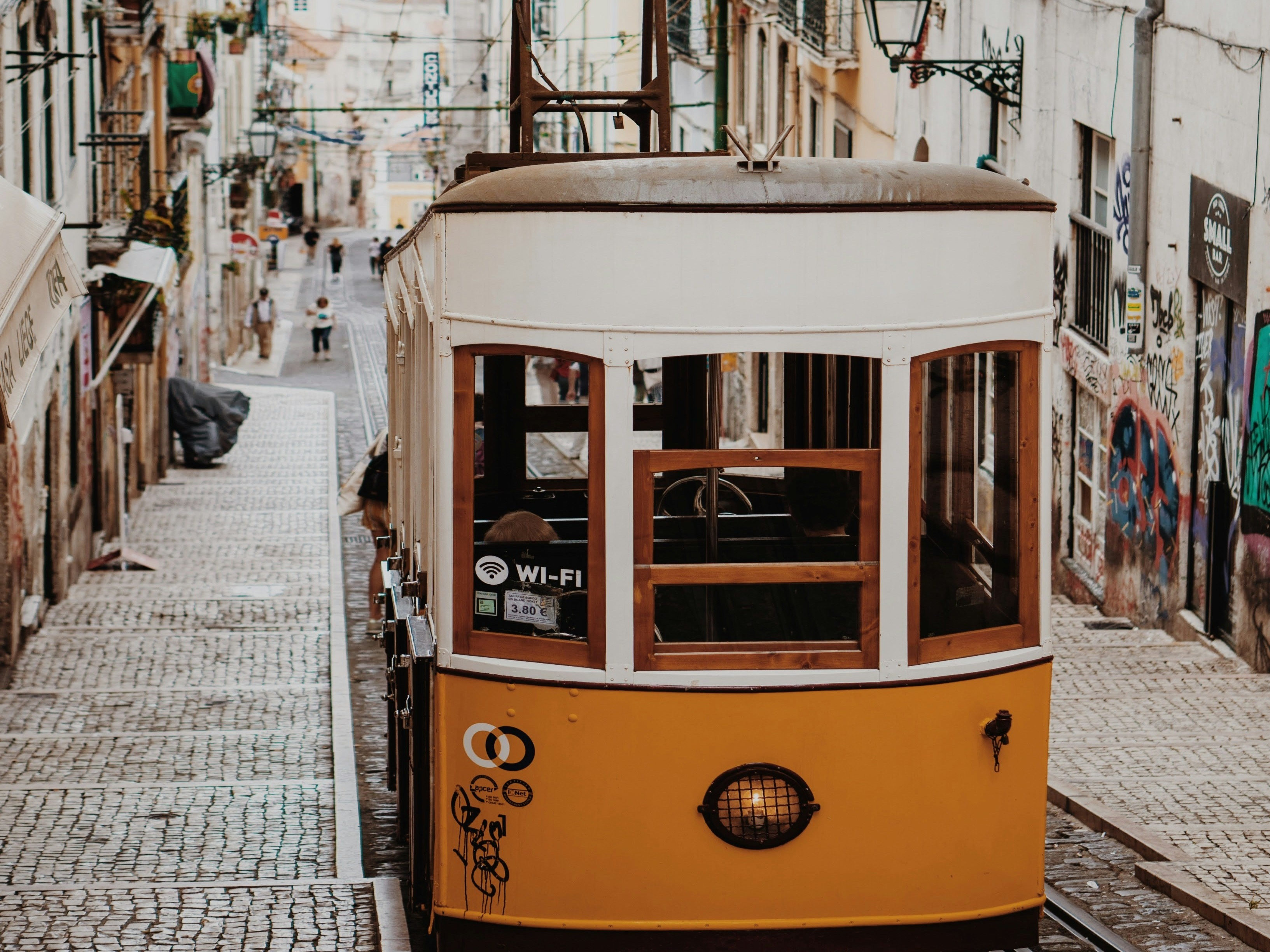 A picture of a yellow & white colored tram in the middle of the road during the daytime.