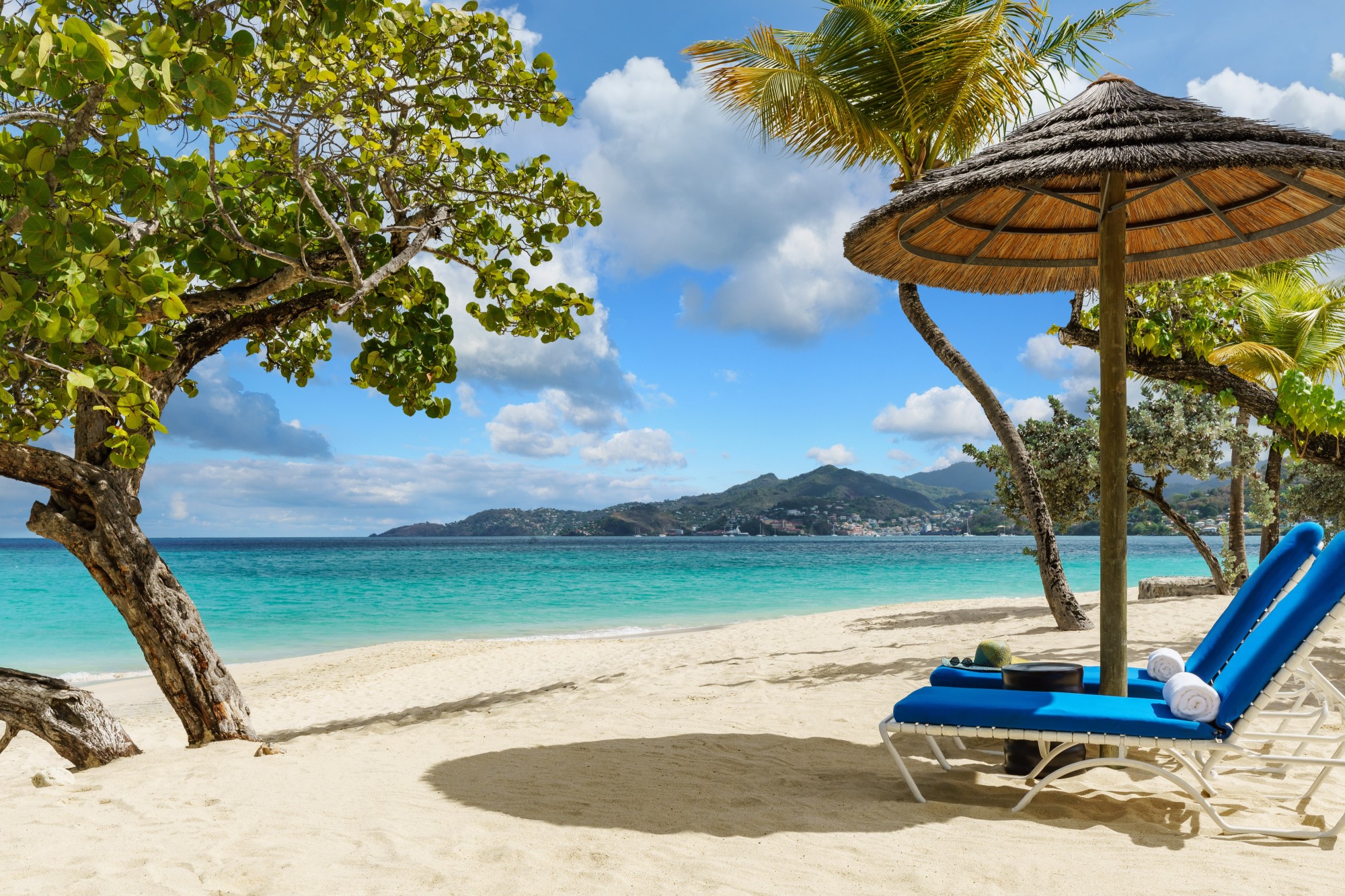 two blue lounge chairs under a straw umbrella overlooking the Caribbean