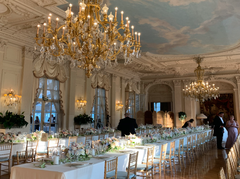 A picture taken of a huge, beautiful dining room table with an large chandeliers hanging from the ceiling.