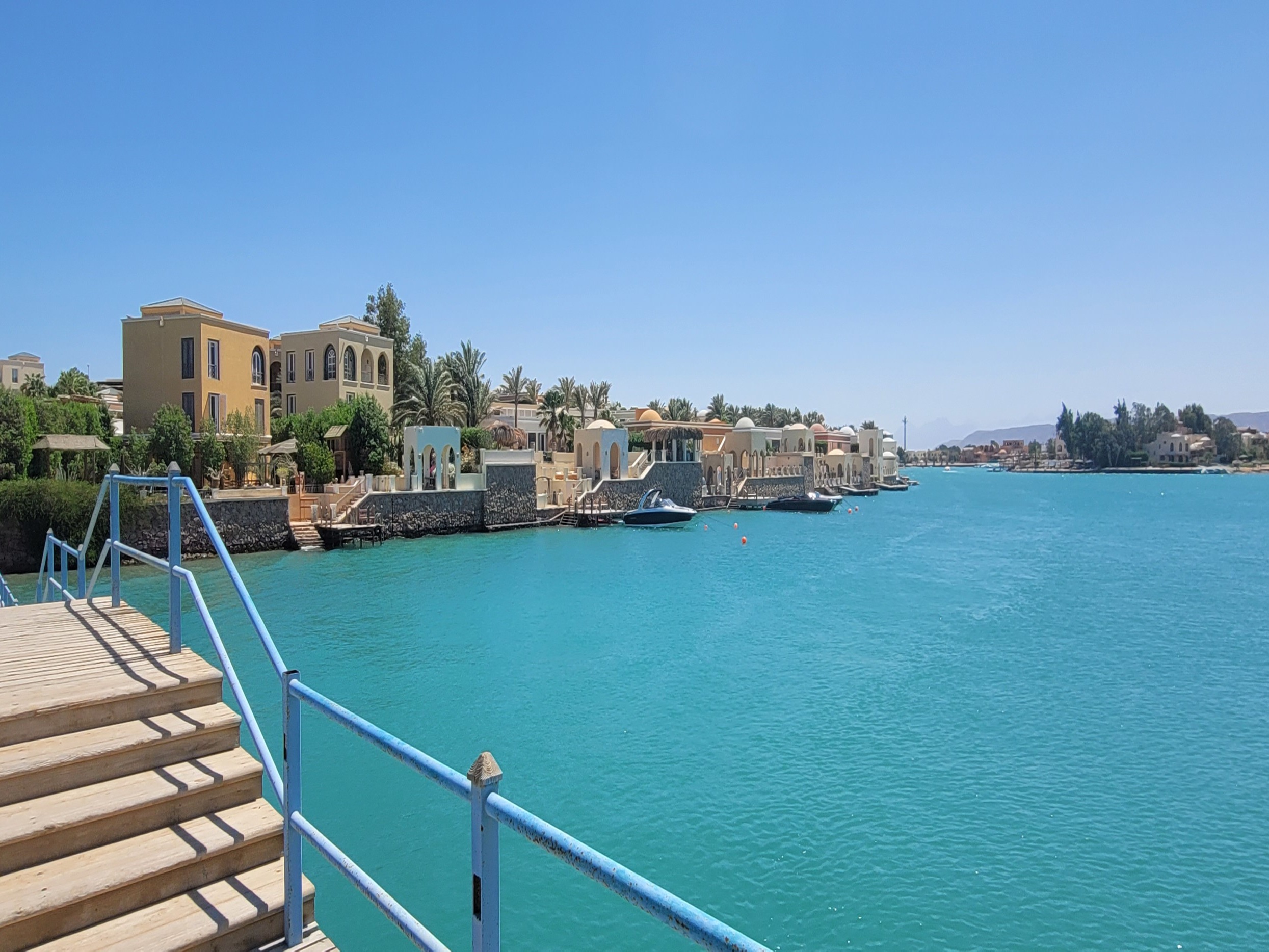 Steps against a blue railing overlooking the turquoise blue water and buildings in the distance.