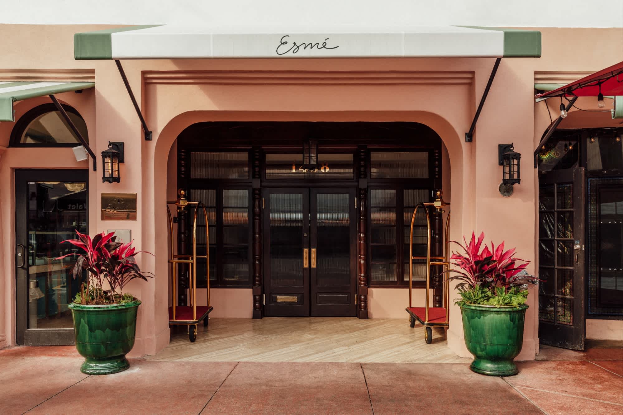 a pink hotel entryway flanked by green clay pots filled with pink plants