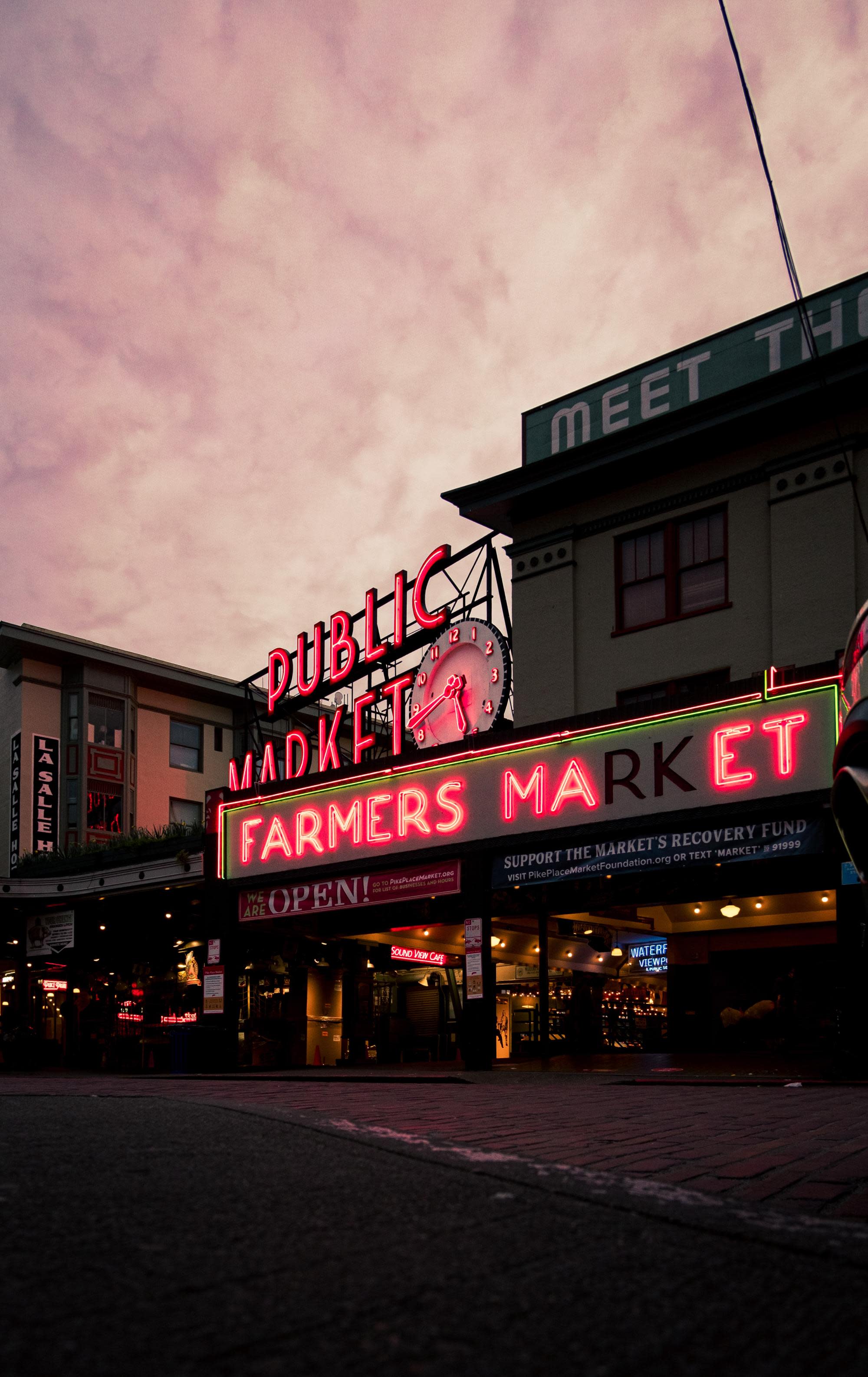 neon sign reads, "public market" and "farmers market" under purple sunset