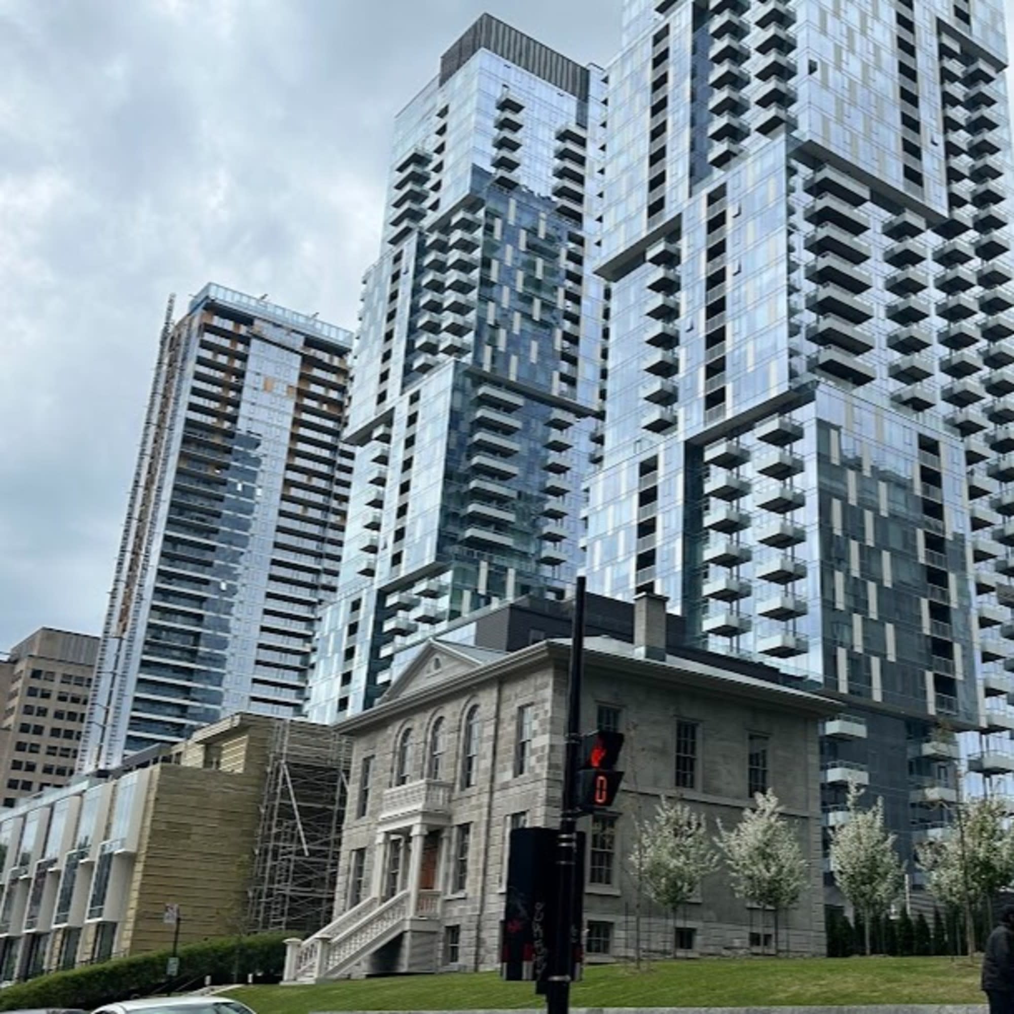 The image shows a classical stone building in the foreground contrasted with modern glass skyscrapers in the background under a cloudy sky.