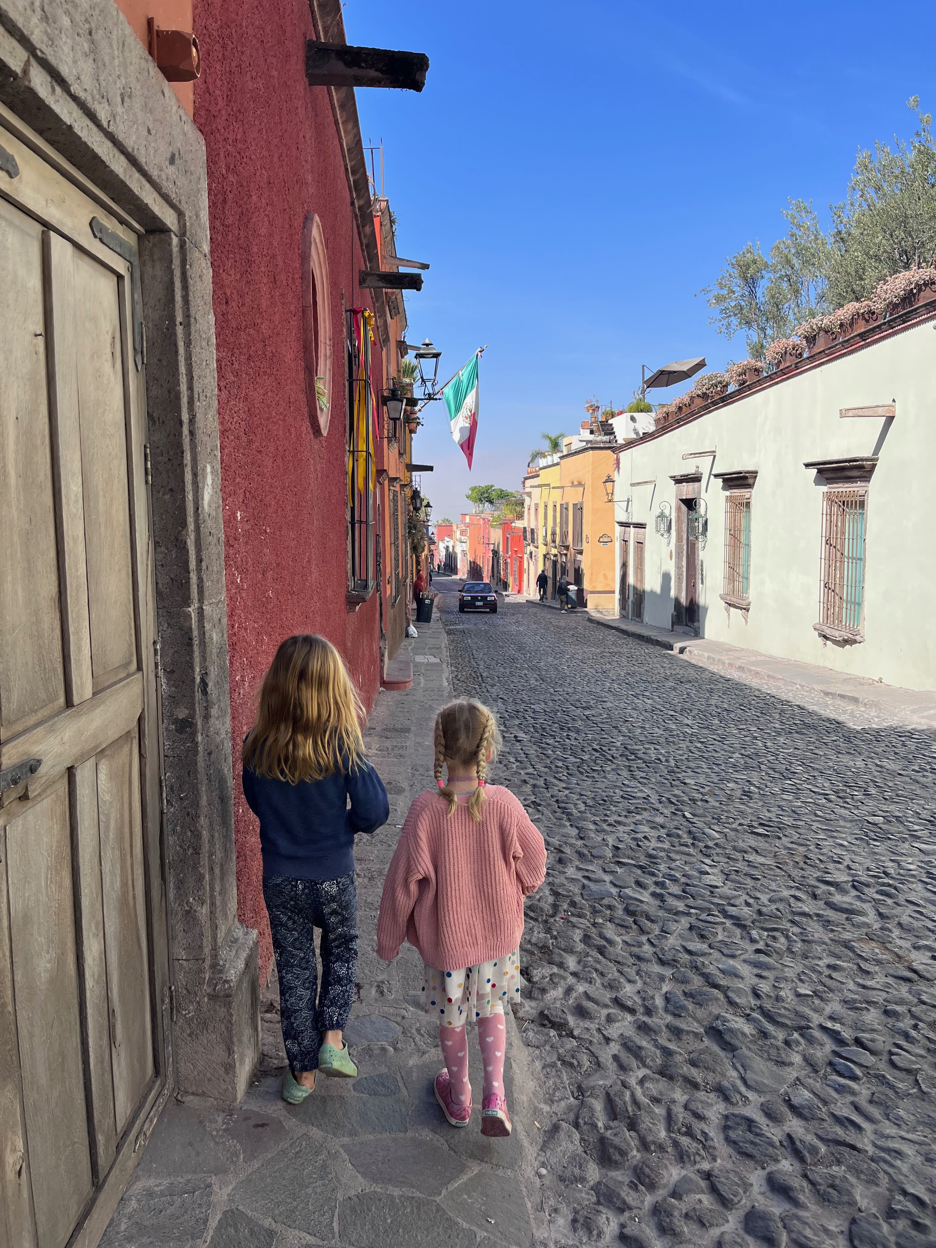 Two children walking down a street with a cobble stone road