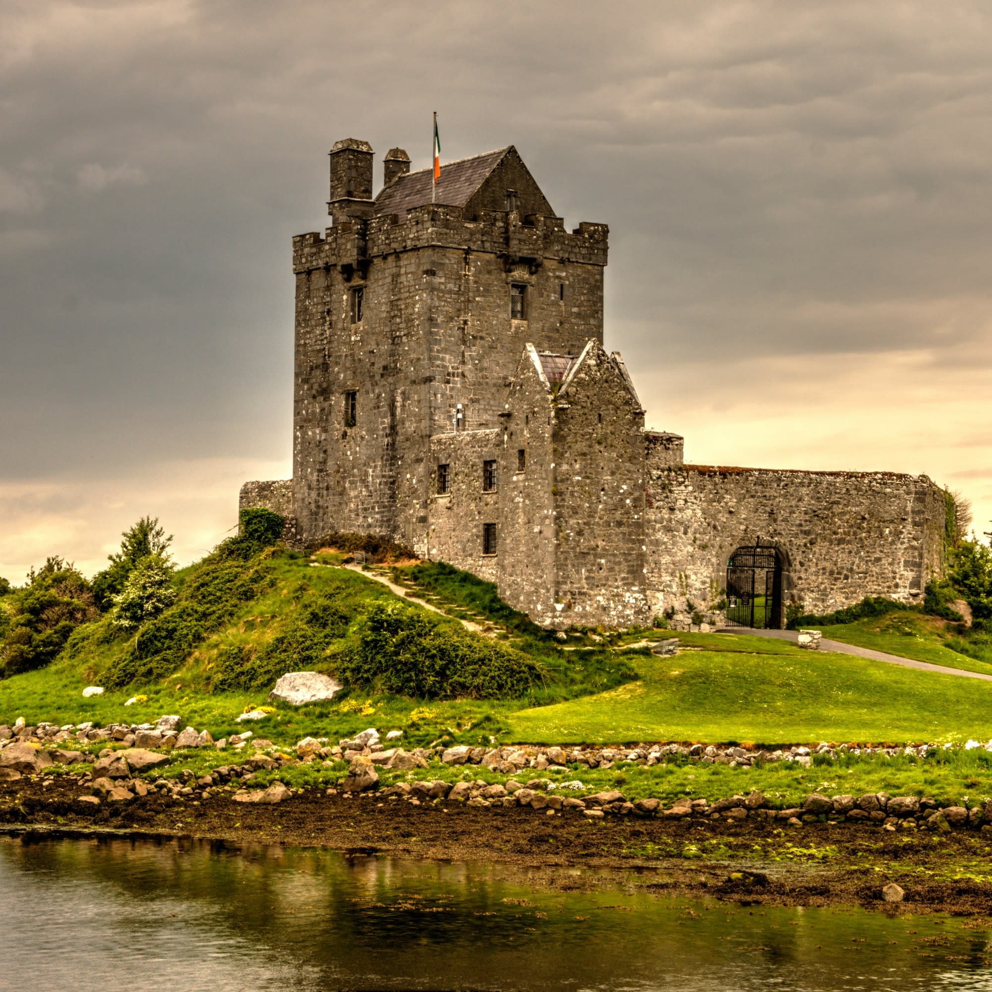 A picture of a gray stone castle by a river in Ireland taken during the daytime.