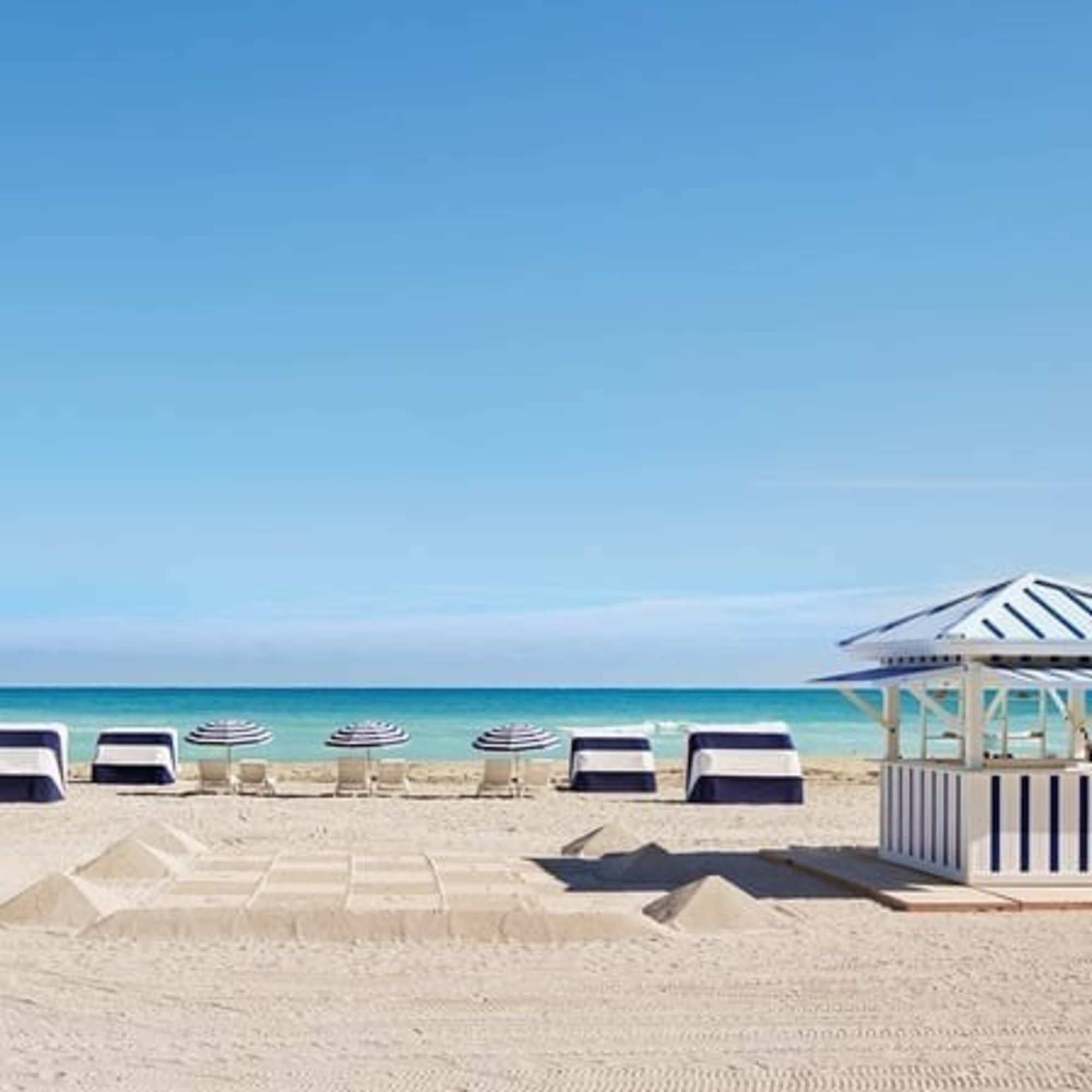 A serene beach scene with white cabanas, lounge chairs, and a clear blue sky.