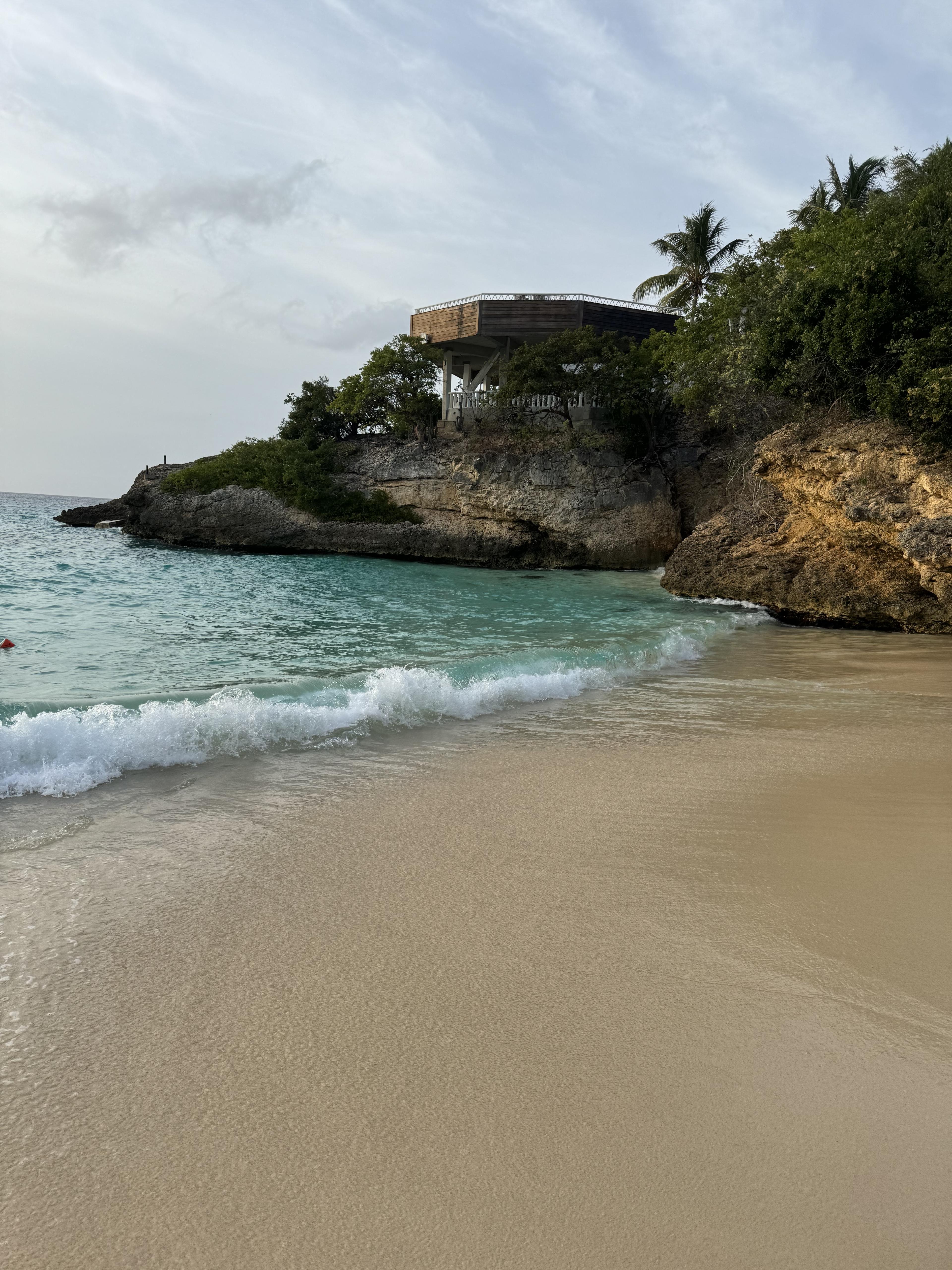 A view of a beach with a rocky formation in view with a small wooden building stucture