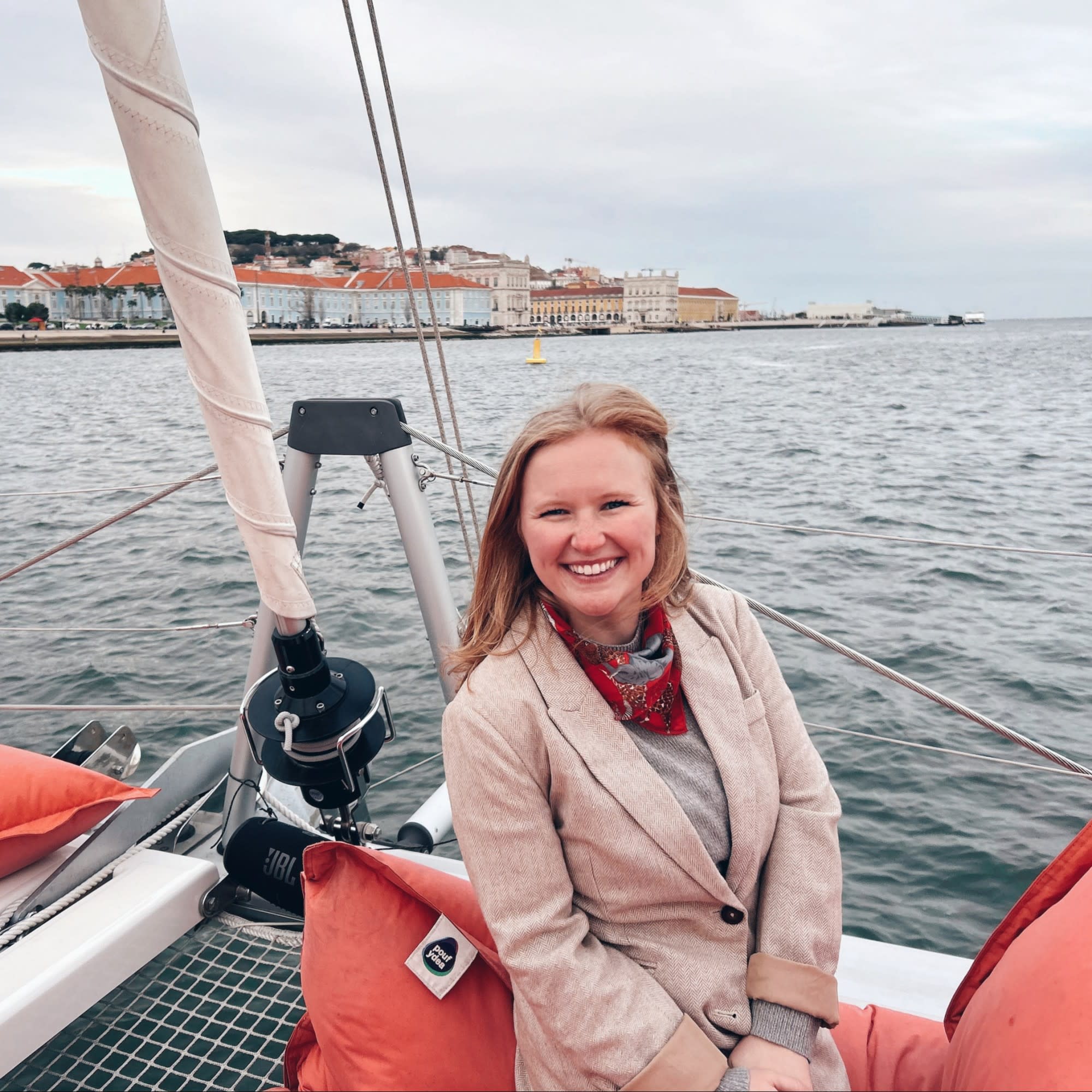 An individual sits on a sailboat, surrounded by water and buildings in the background.